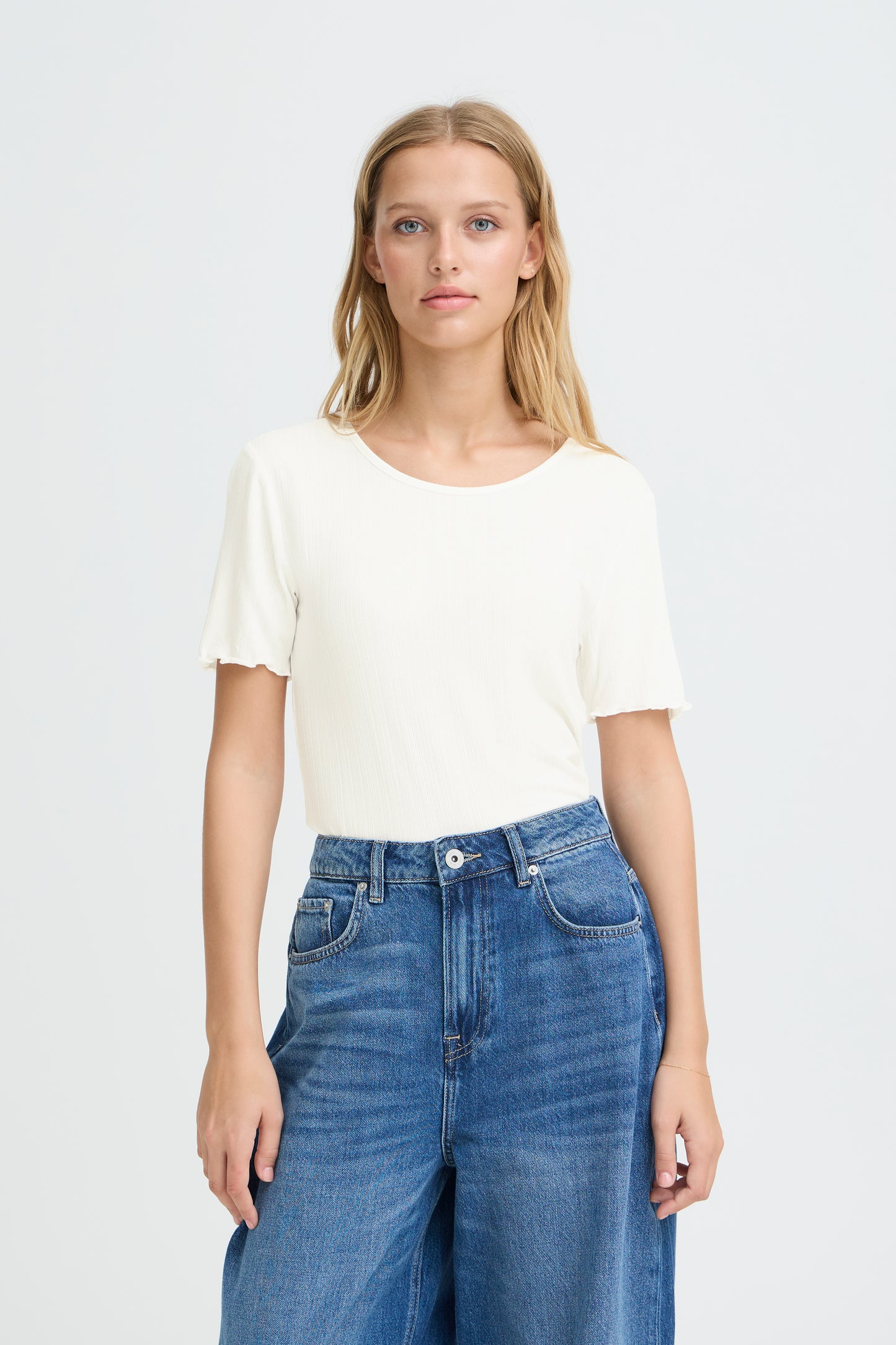 Woman wearing a white t-shirt and blue jeans on a plain background
