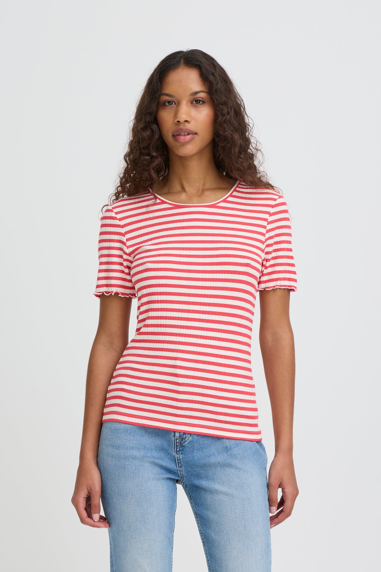 Woman wearing a red and white striped shirt and blue jeans on a plain background