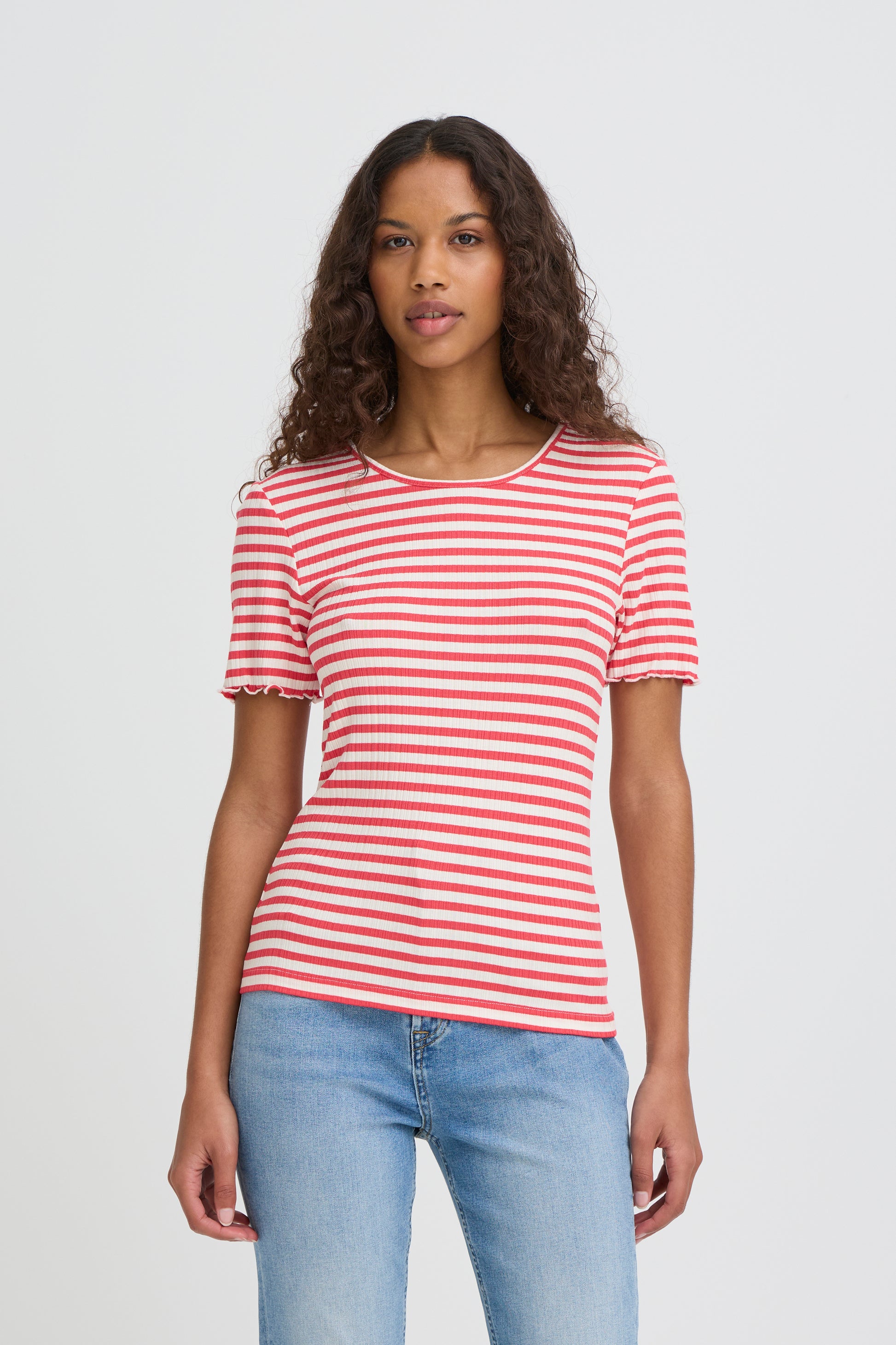 Woman wearing a red and white striped shirt and blue jeans on a plain background