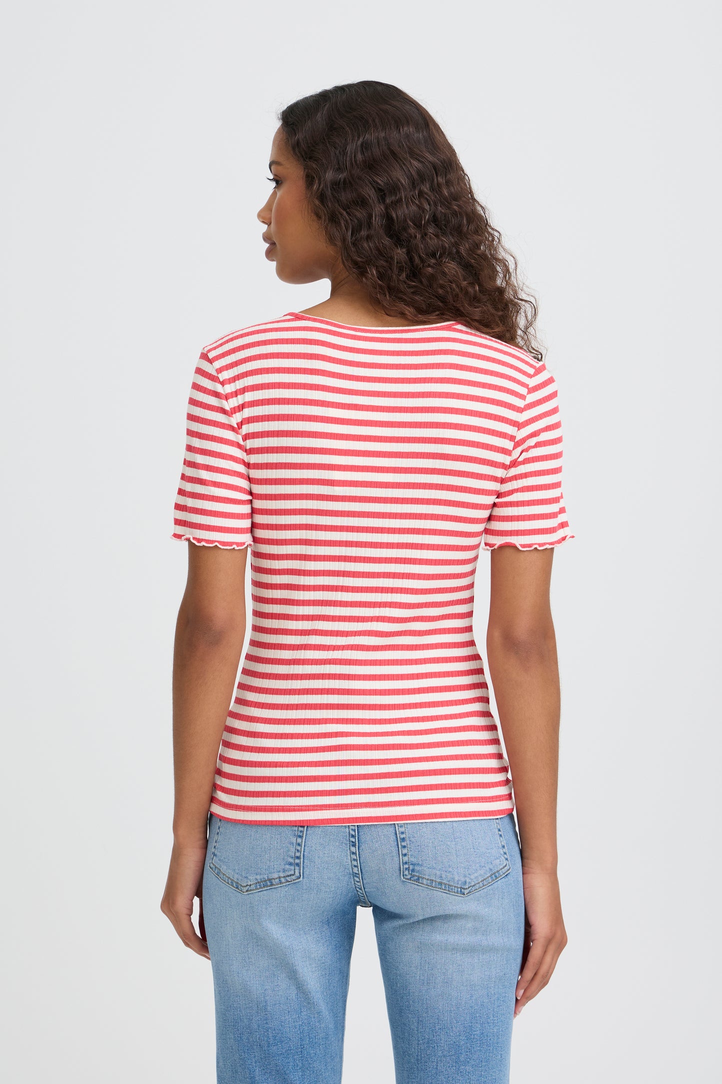 Woman wearing a red and white striped shirt and blue jeans on a light gray background