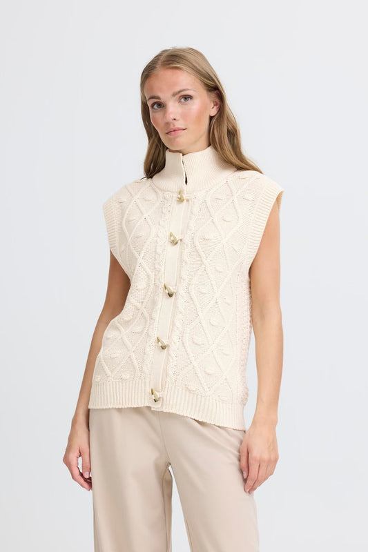 Woman wearing a cream-colored cable knit vest on a white background