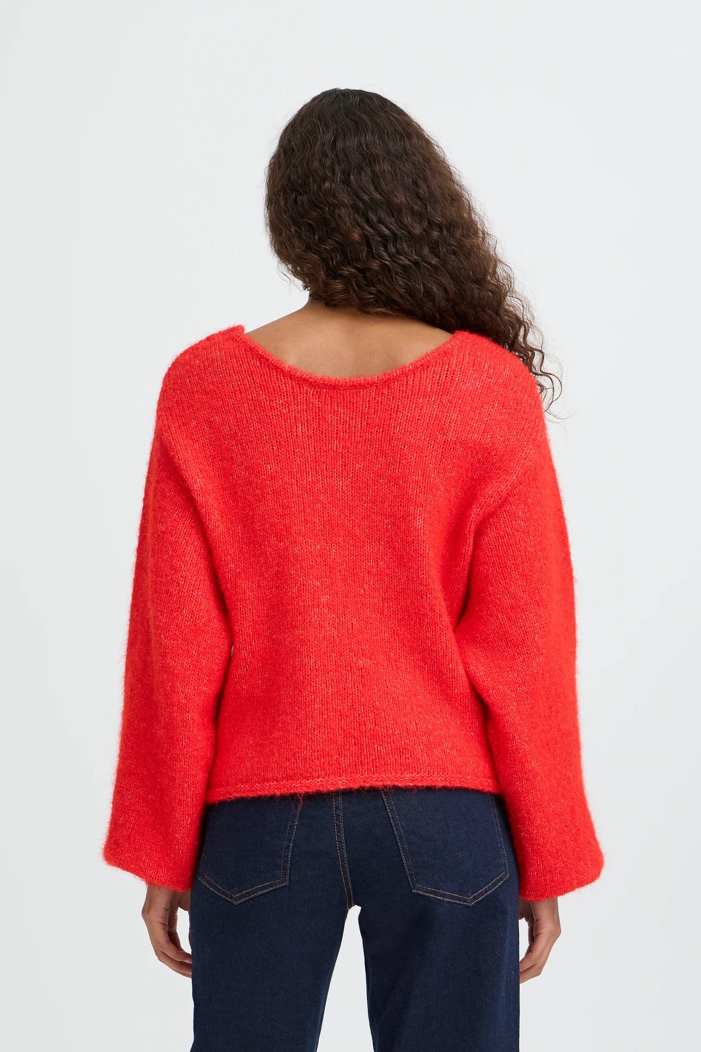 Person wearing a red sweater and dark jeans on a white background
