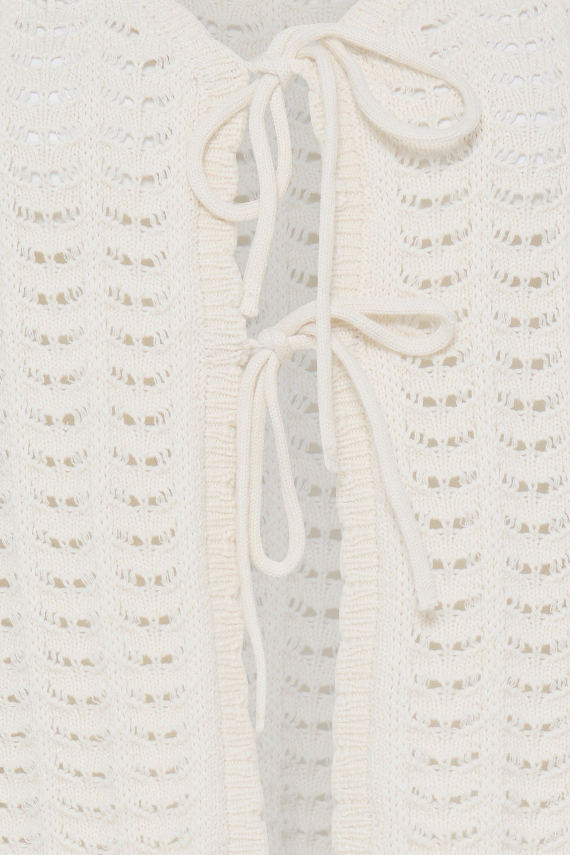 Close-up of a textured white garment with a tie detail on a light gray background