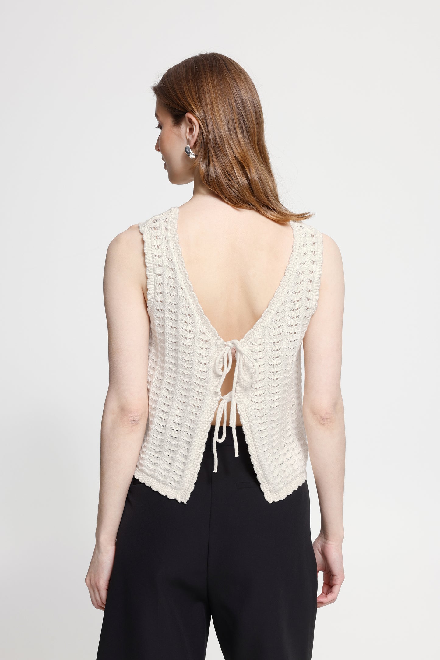 Woman wearing a white crochet top with an open back on a plain background