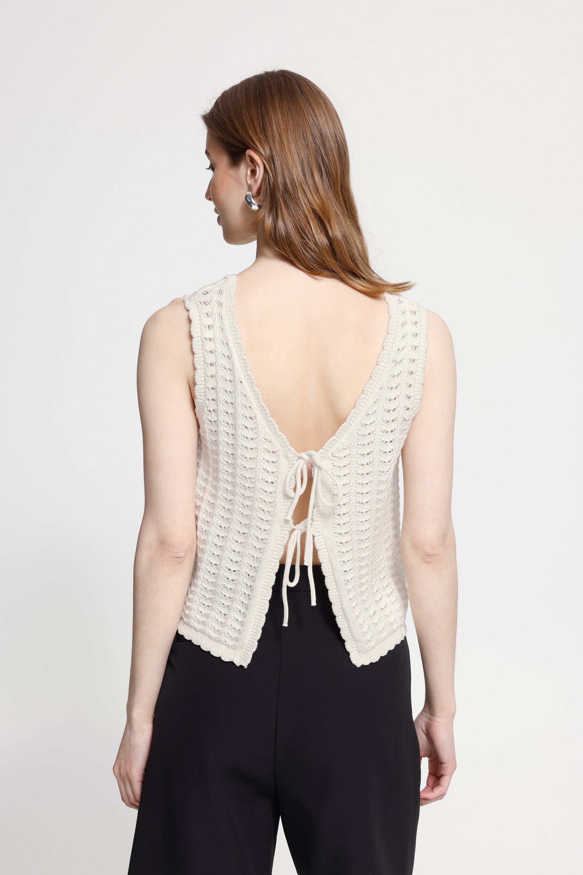 Woman wearing a white crochet top with an open back on a plain background