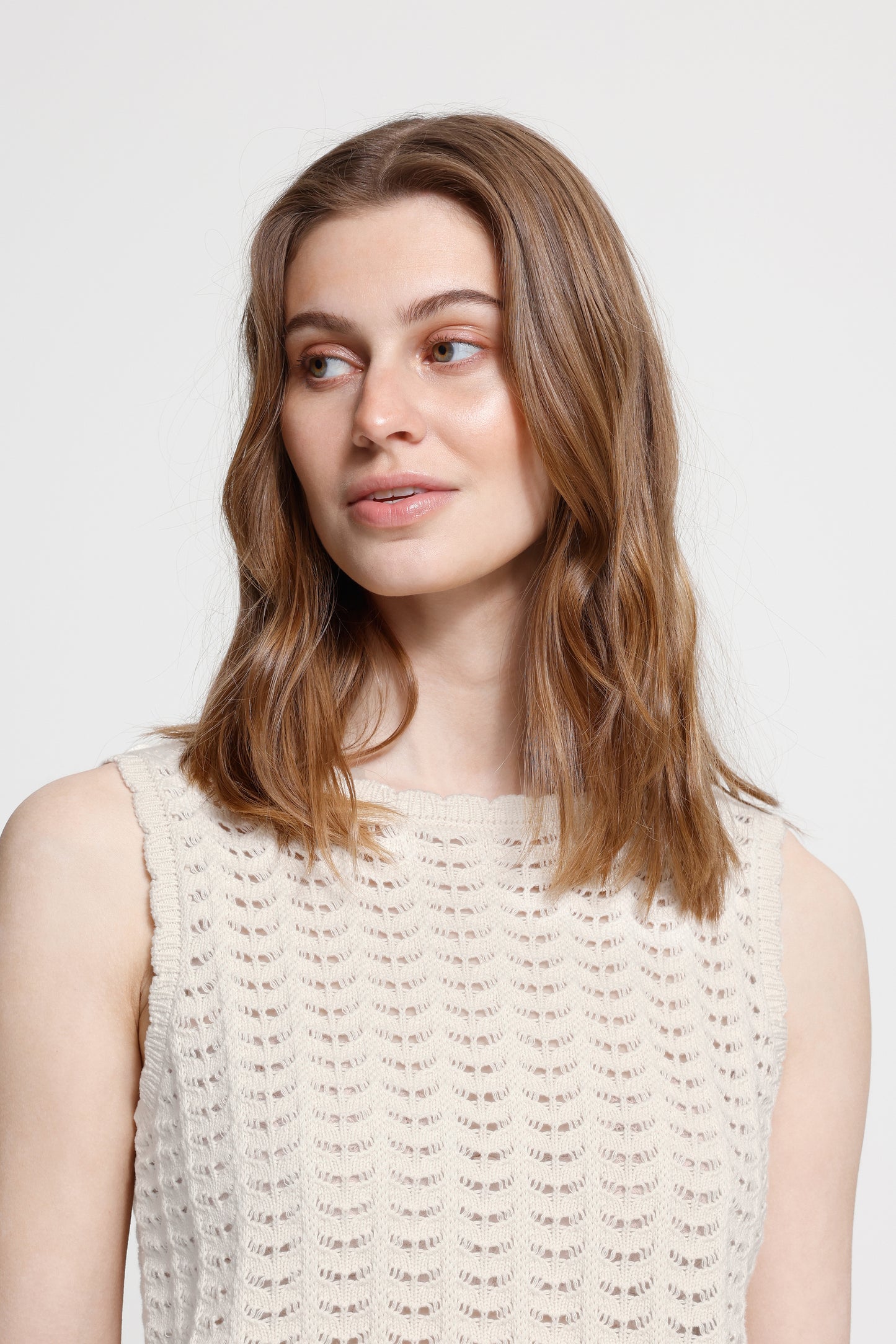 Woman with shoulder-length brown hair wearing a light-colored sleeveless top against a plain background