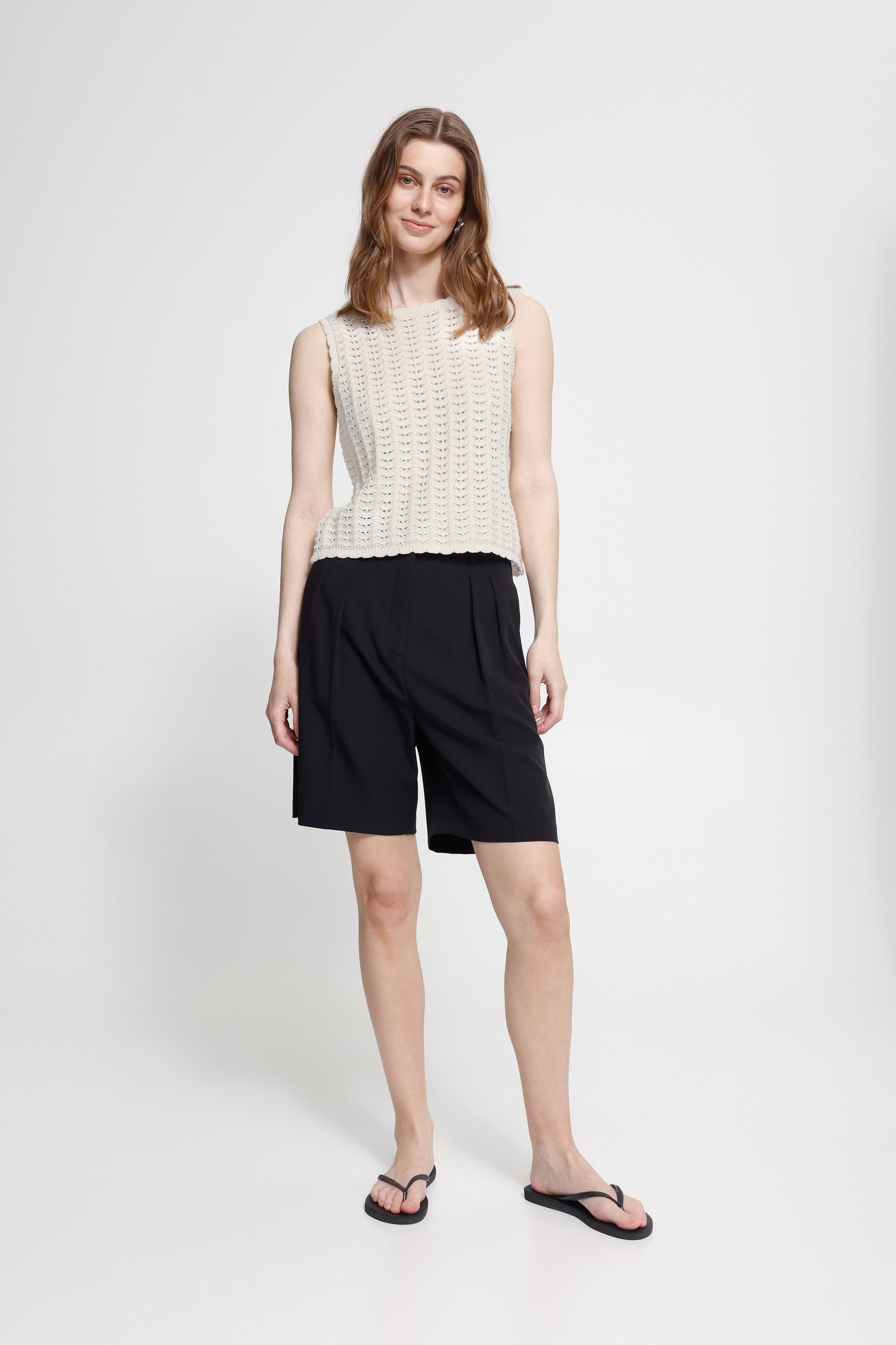 Woman wearing a white sleeveless top and black shorts on a white background