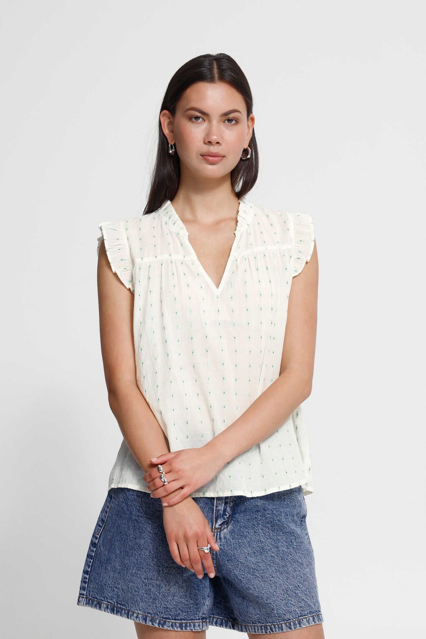Woman wearing a white sleeveless top and denim shorts on a plain background