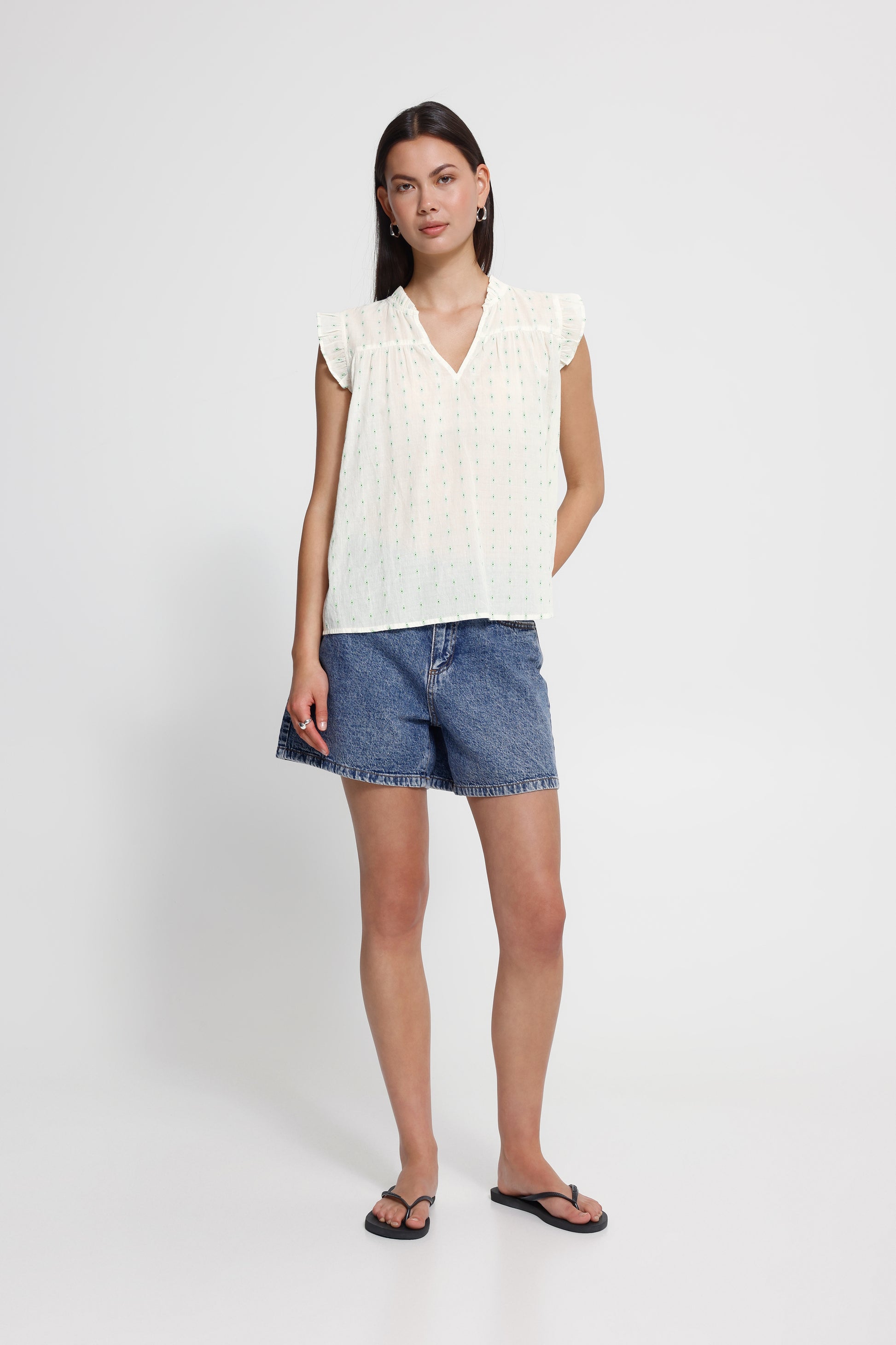 Woman wearing a white sleeveless top and denim shorts on a white background