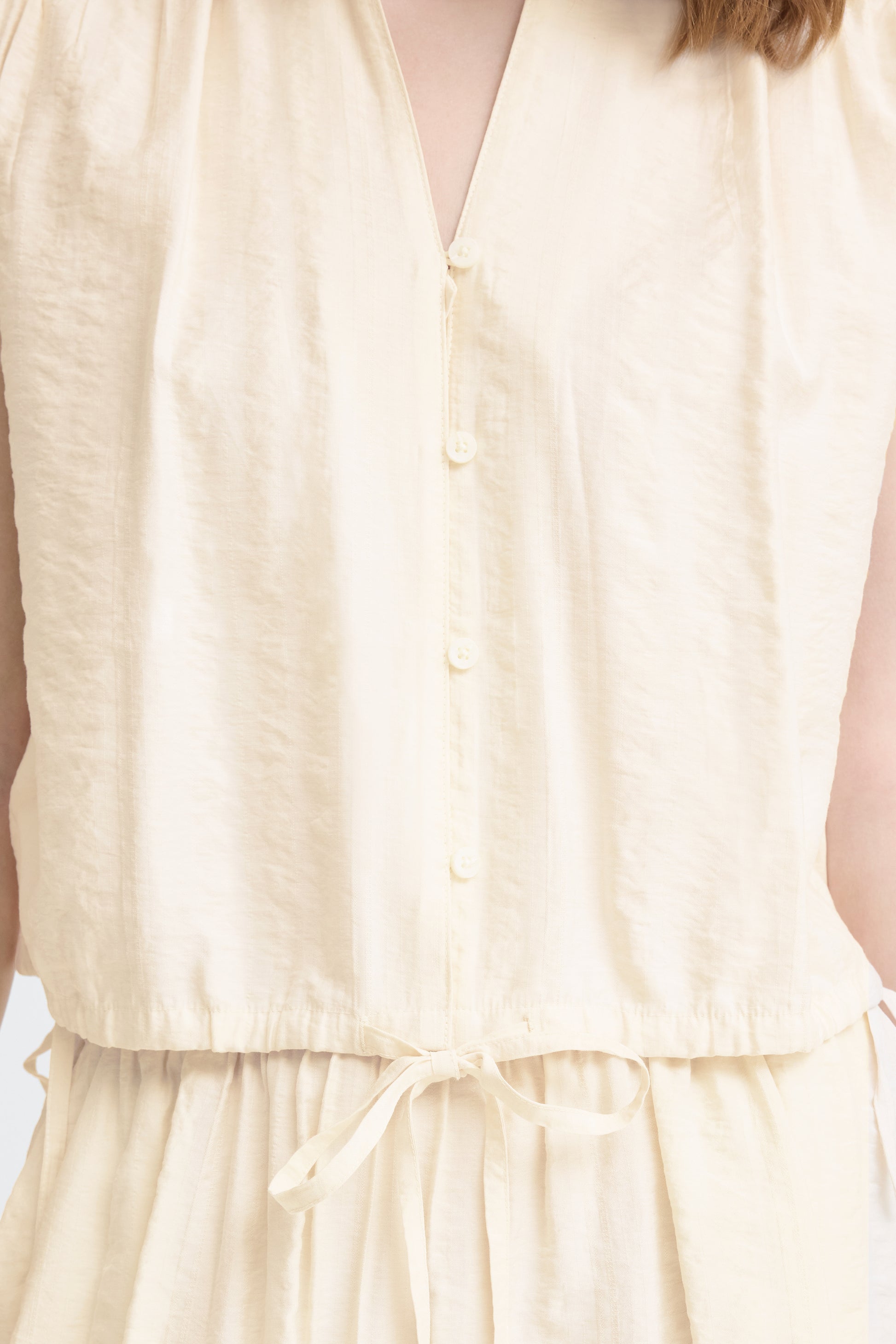 Close-up of a beige sleeveless top with buttons and a tie waist.