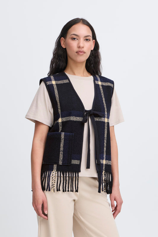 Woman wearing a navy plaid vest with fringe on a white background