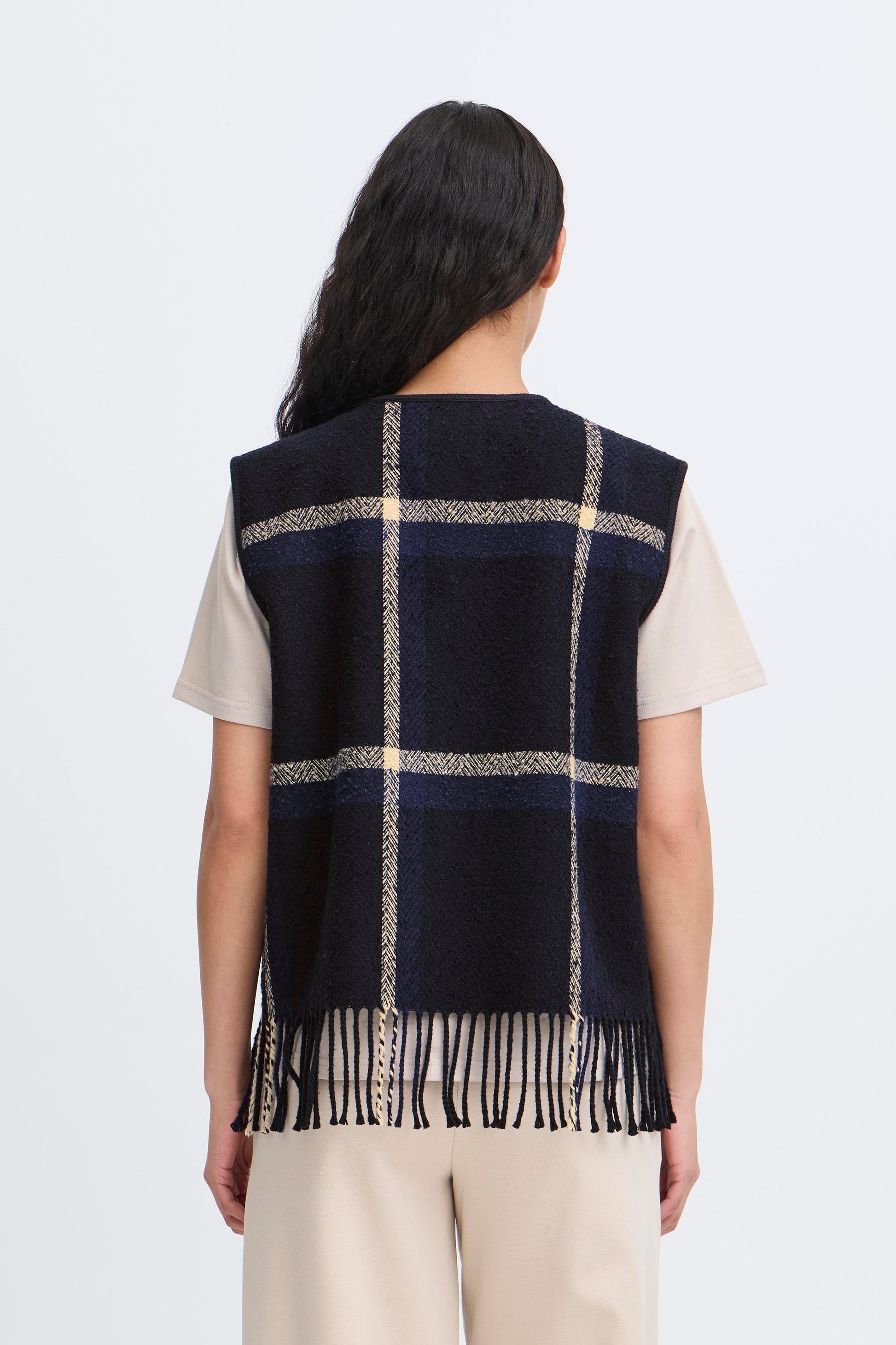Person wearing a navy checkered vest with fringes on a white background