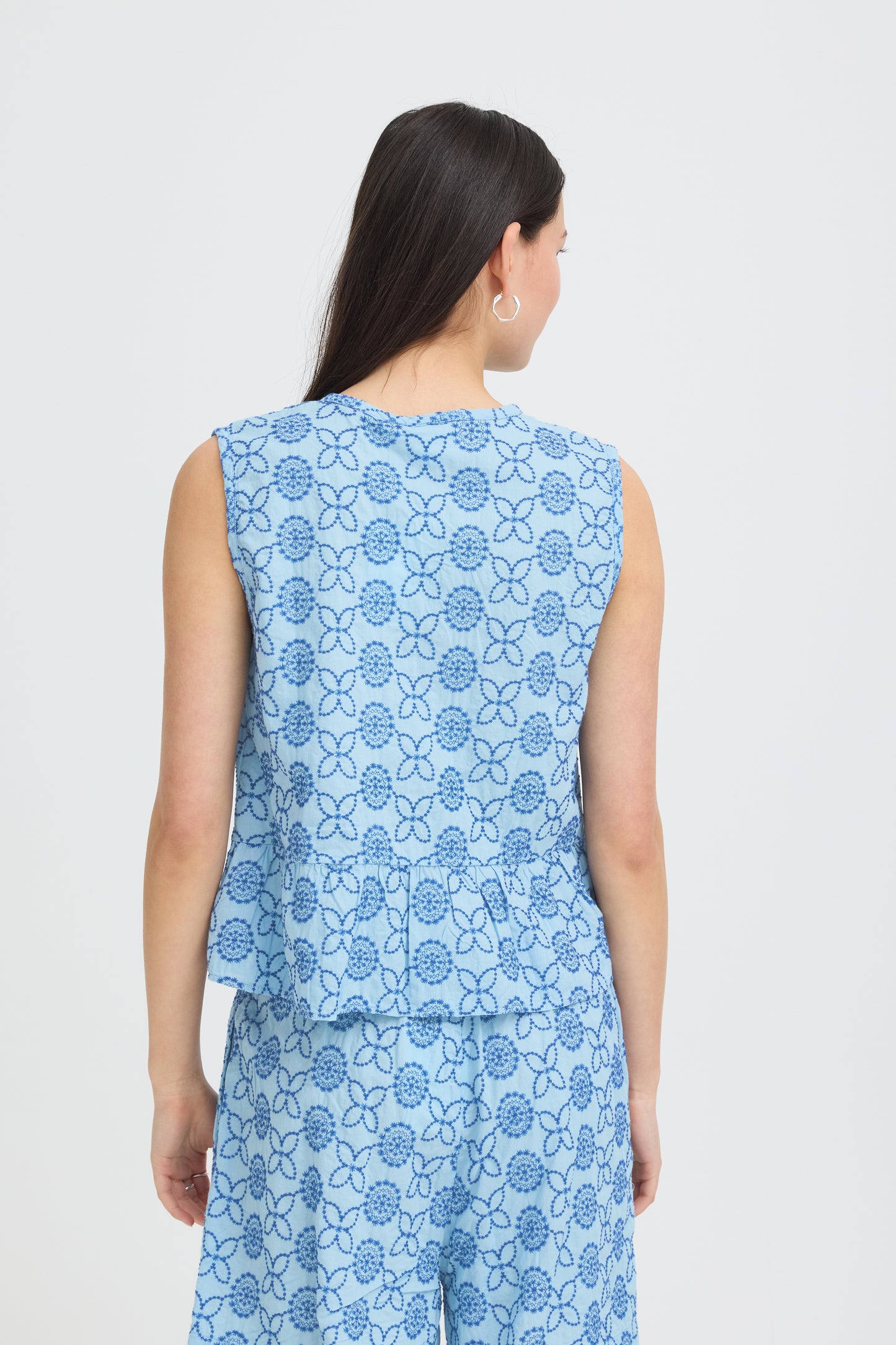 Woman wearing a blue floral sleeveless top and pants on a white background