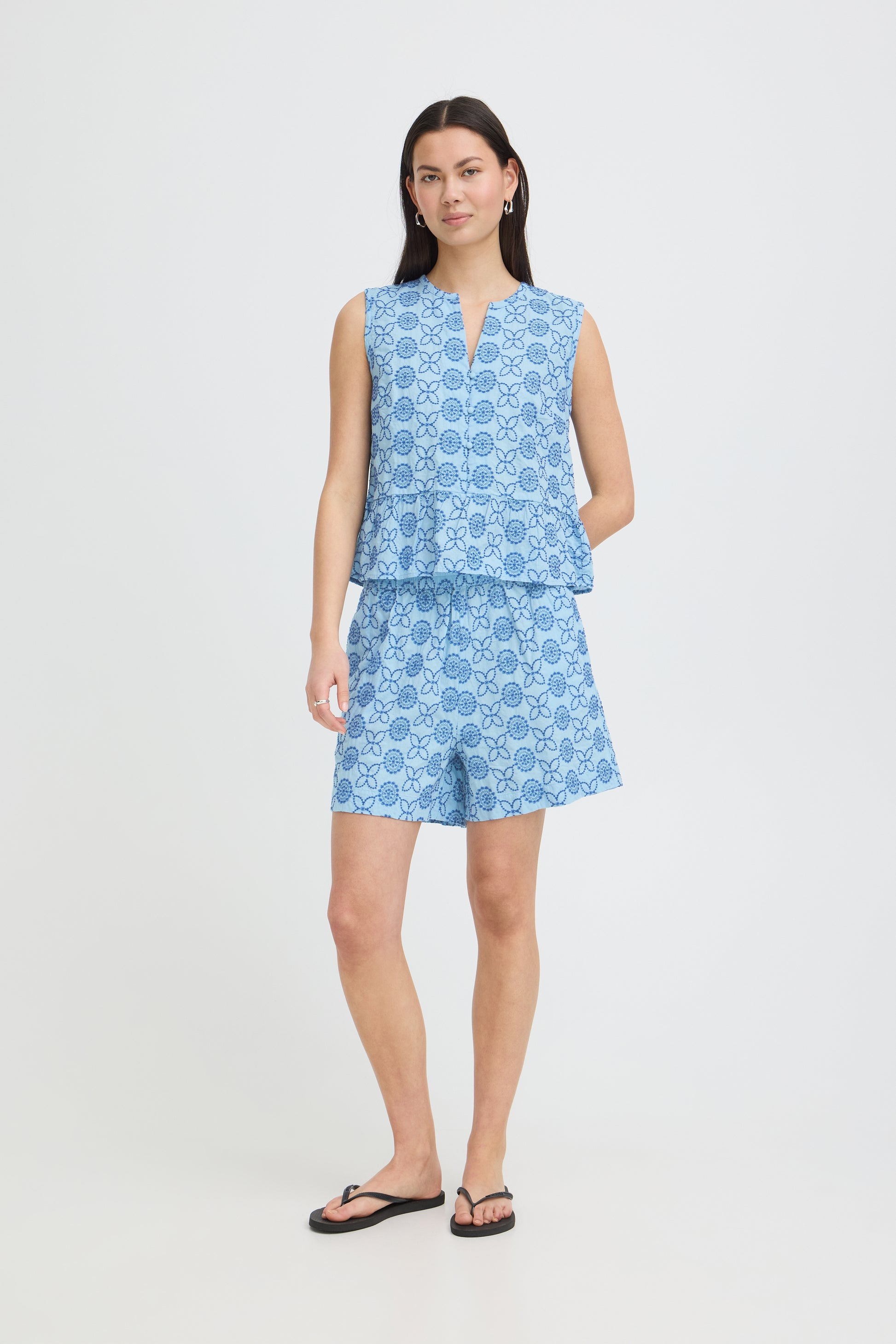 Woman wearing a blue patterned sleeveless top and shorts on a white background