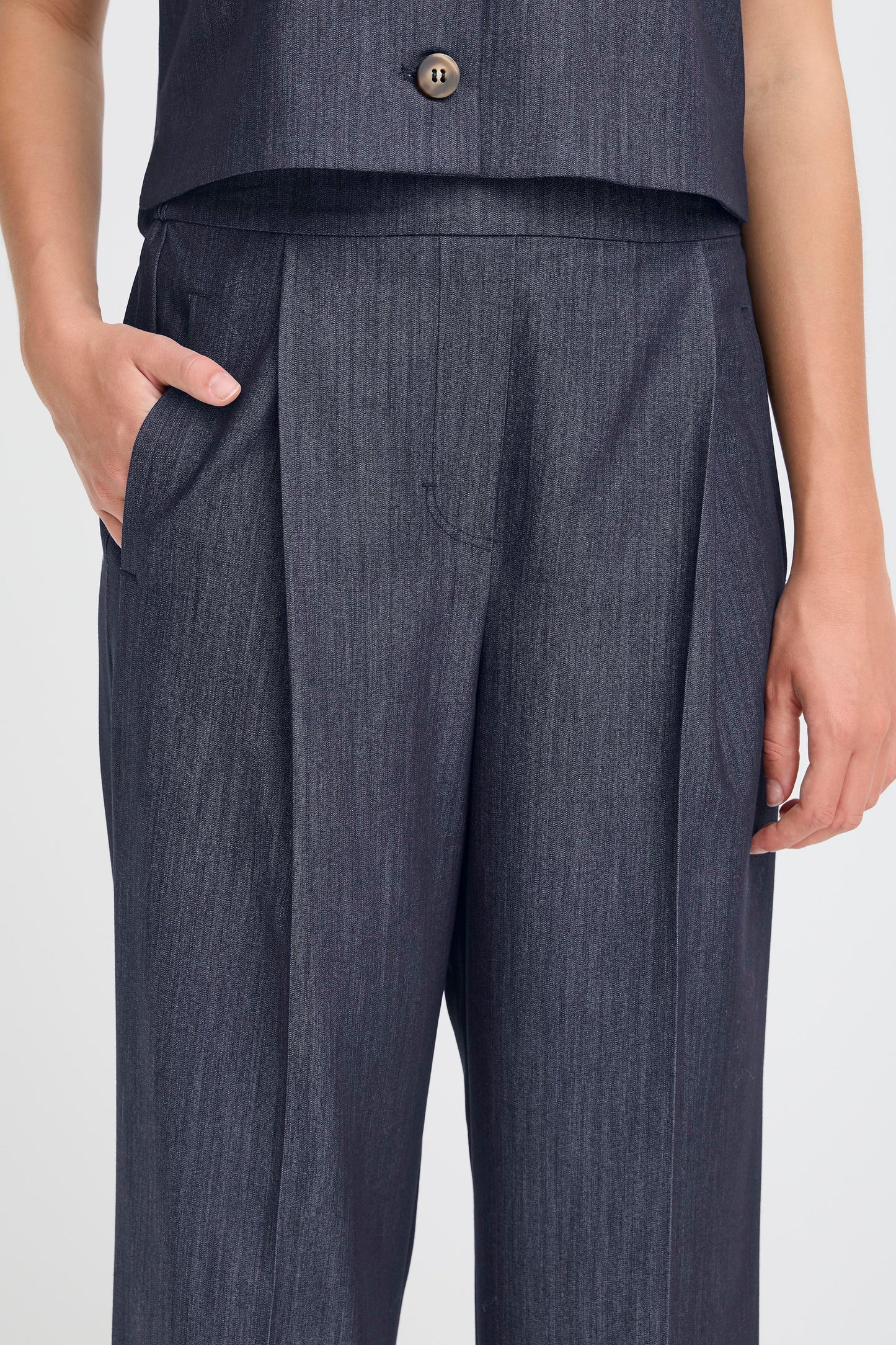 Dark blue pleated pants worn by a person on a white background