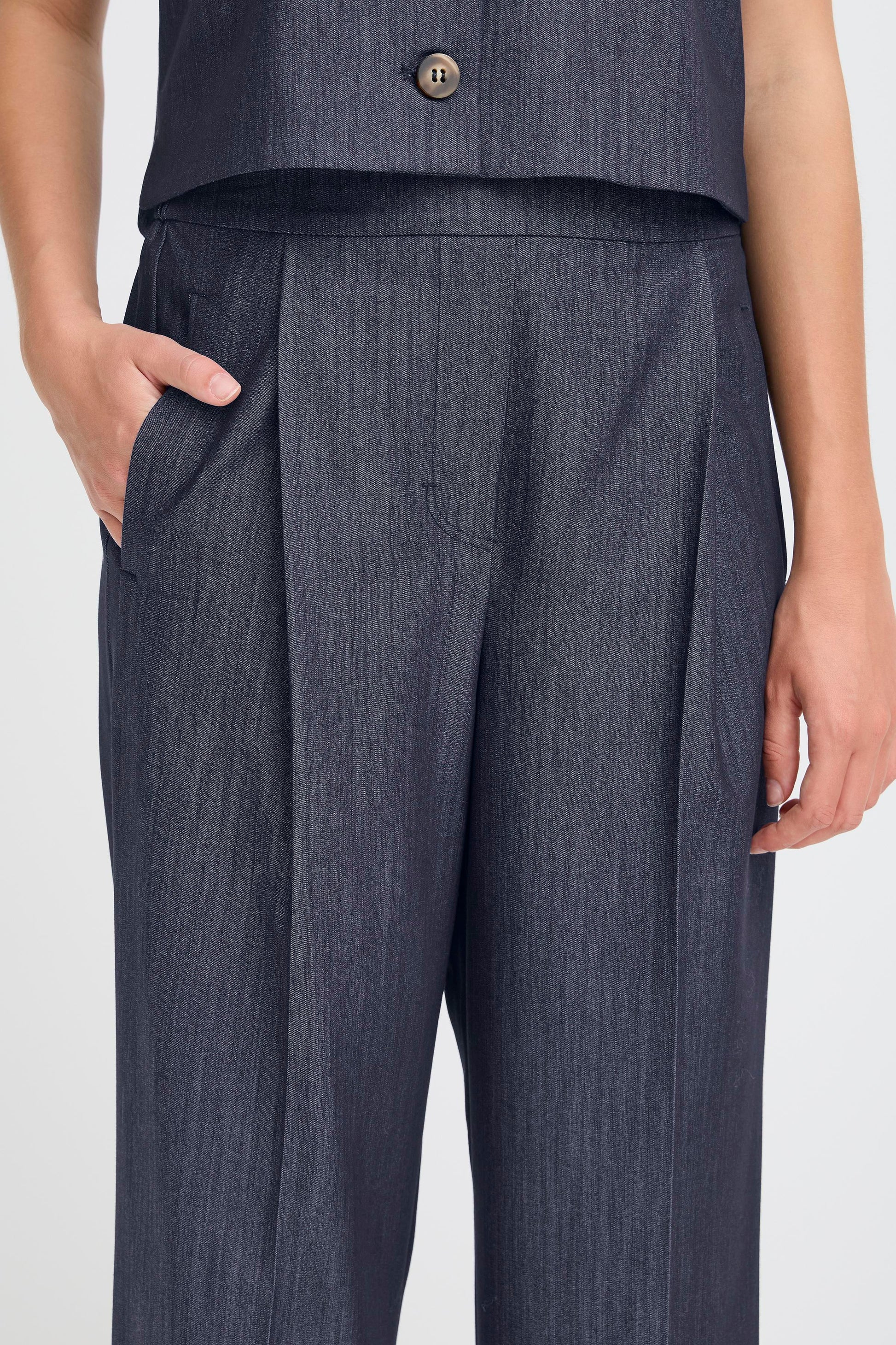 Dark blue pleated pants worn by a person on a white background