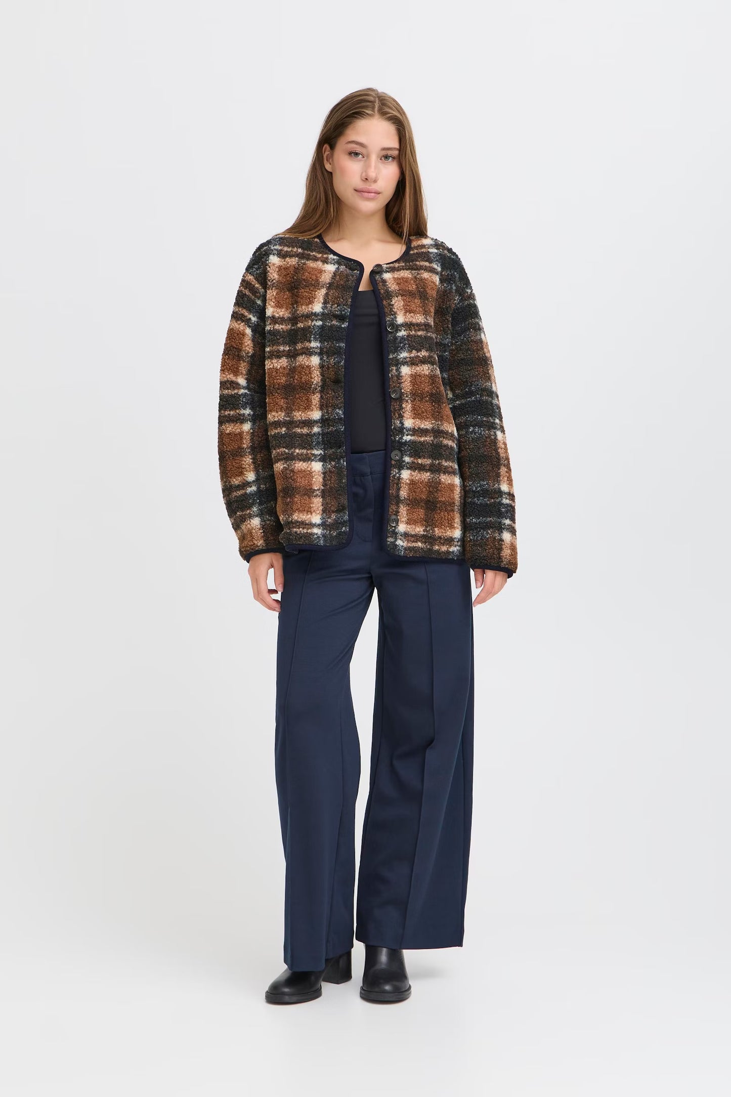 Woman wearing a plaid jacket and navy pants on a white background