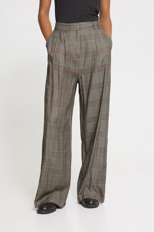 A person wearing high-waisted, wide-leg plaid trousers in a muted olive-gray color with thin red and beige windowpane lines, paired with a black top and black shoes, against a plain white studio background.