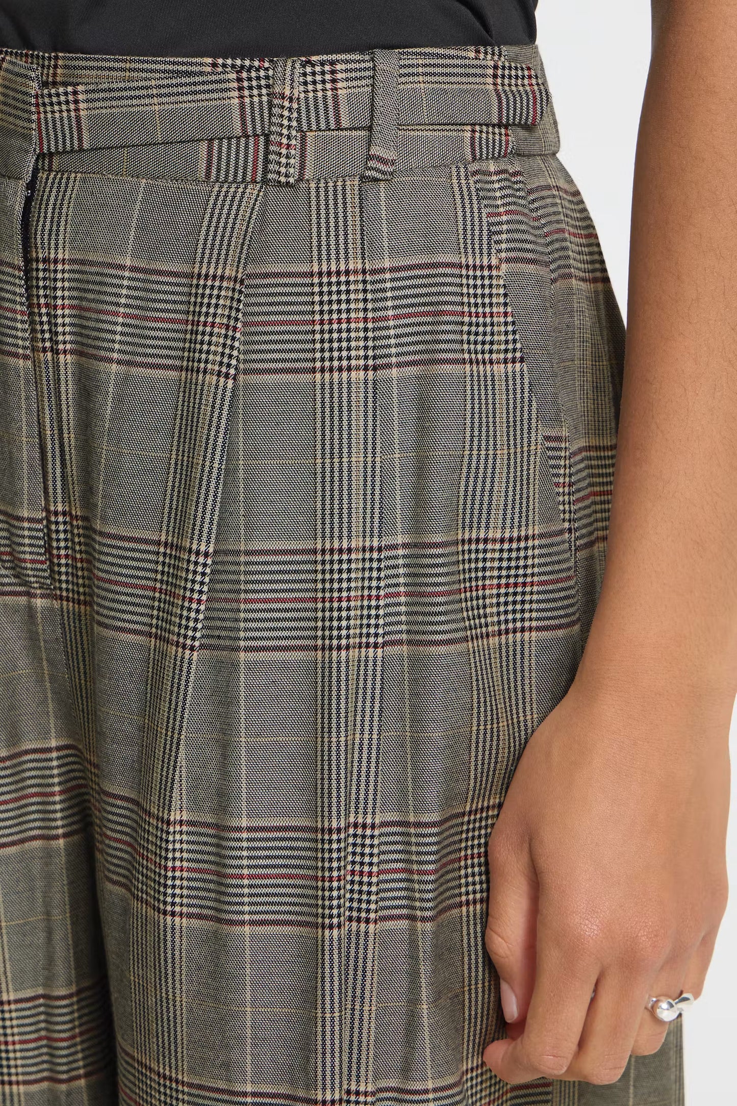 Close-up of a person wearing gray plaid trousers with a belt, showing the fabric pattern and part of the hand wearing a ring.