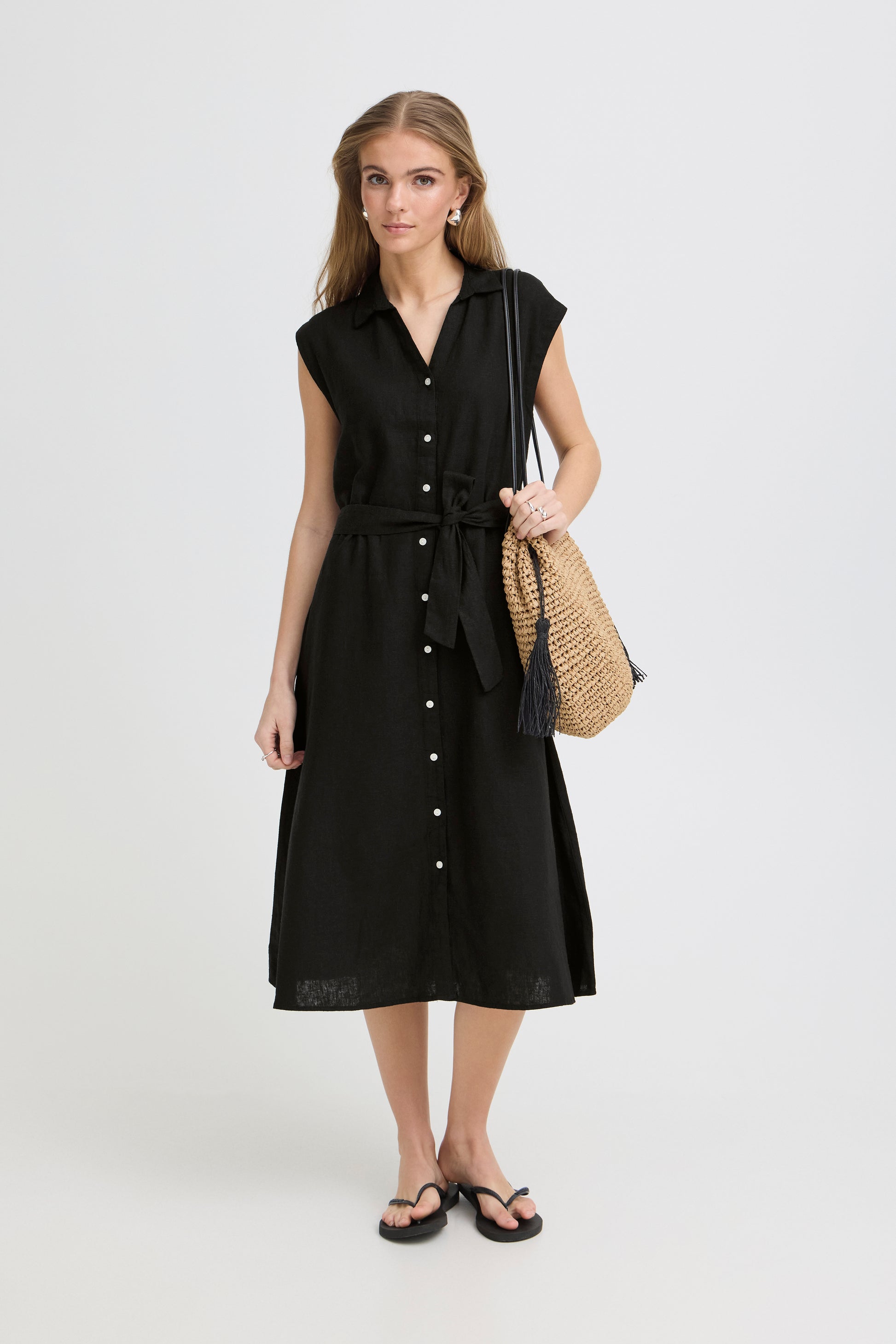 Woman wearing a black sleeveless dress with buttons on a white background