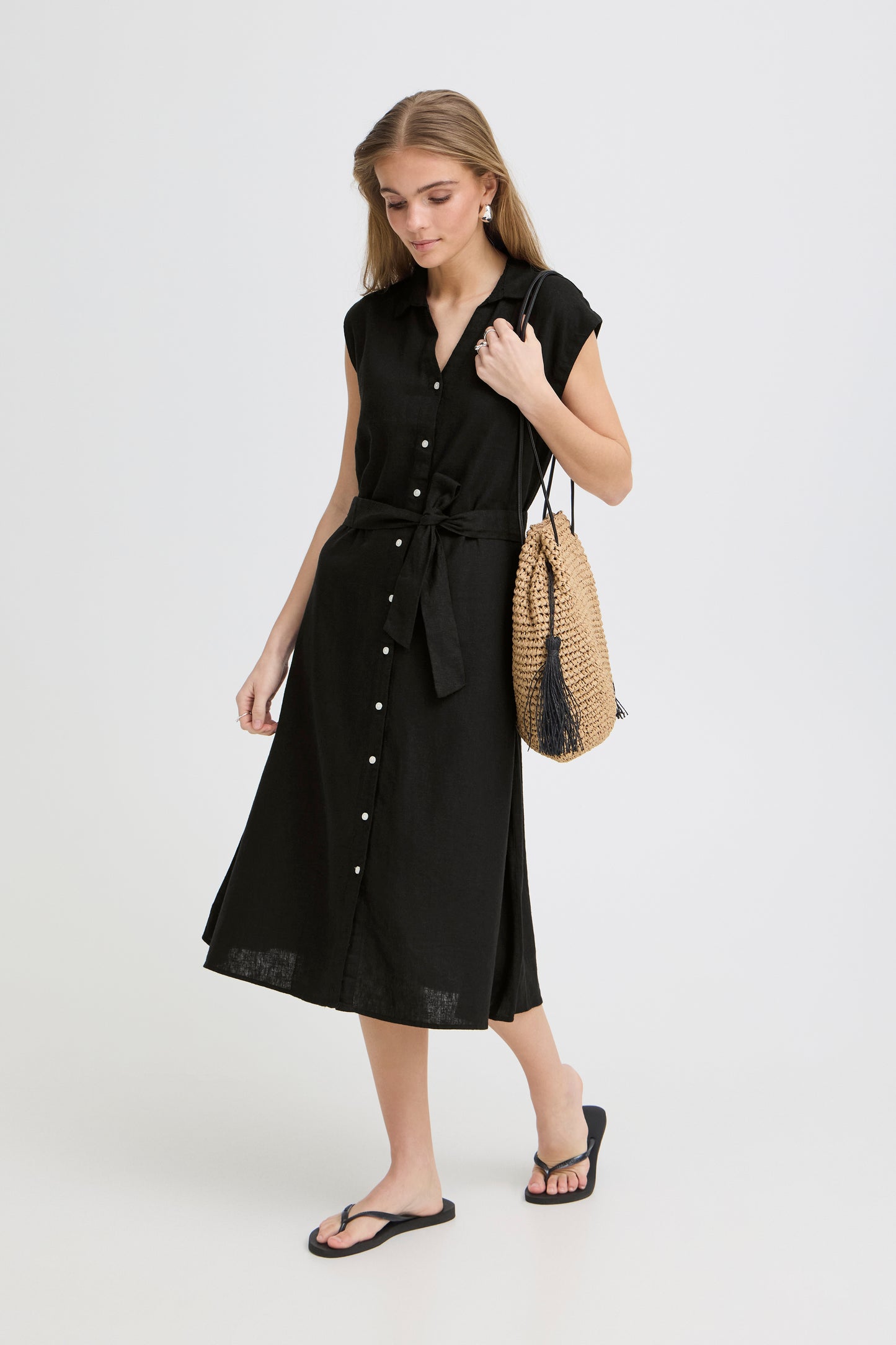 Woman wearing a black sleeveless dress holding a straw bag on a white background