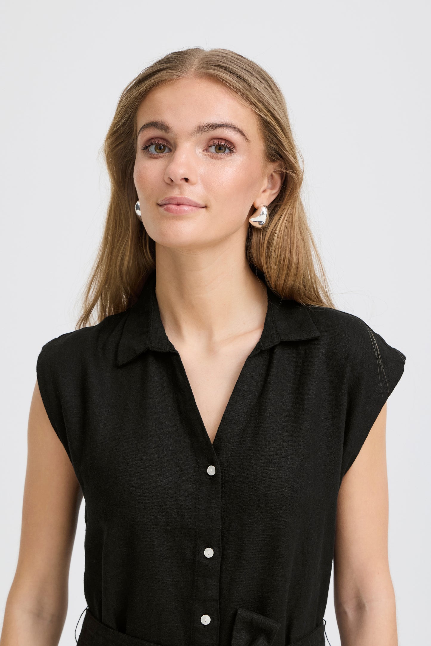 Woman wearing a black sleeveless blouse with white buttons on a plain background