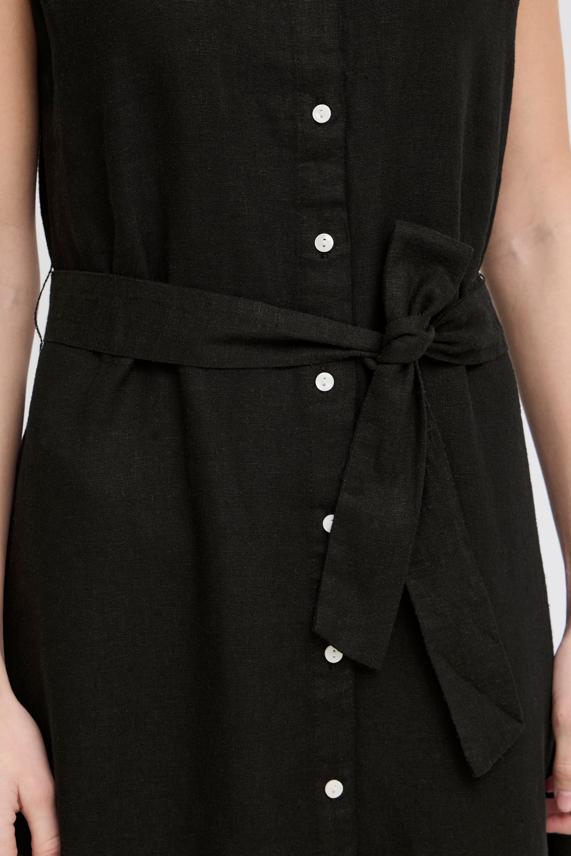 Black sleeveless dress with buttons and a tie waist on a white background