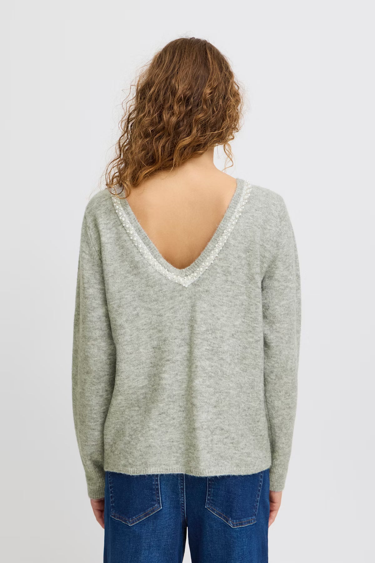 Person wearing a light gray sweater with a lace neckline on a white background