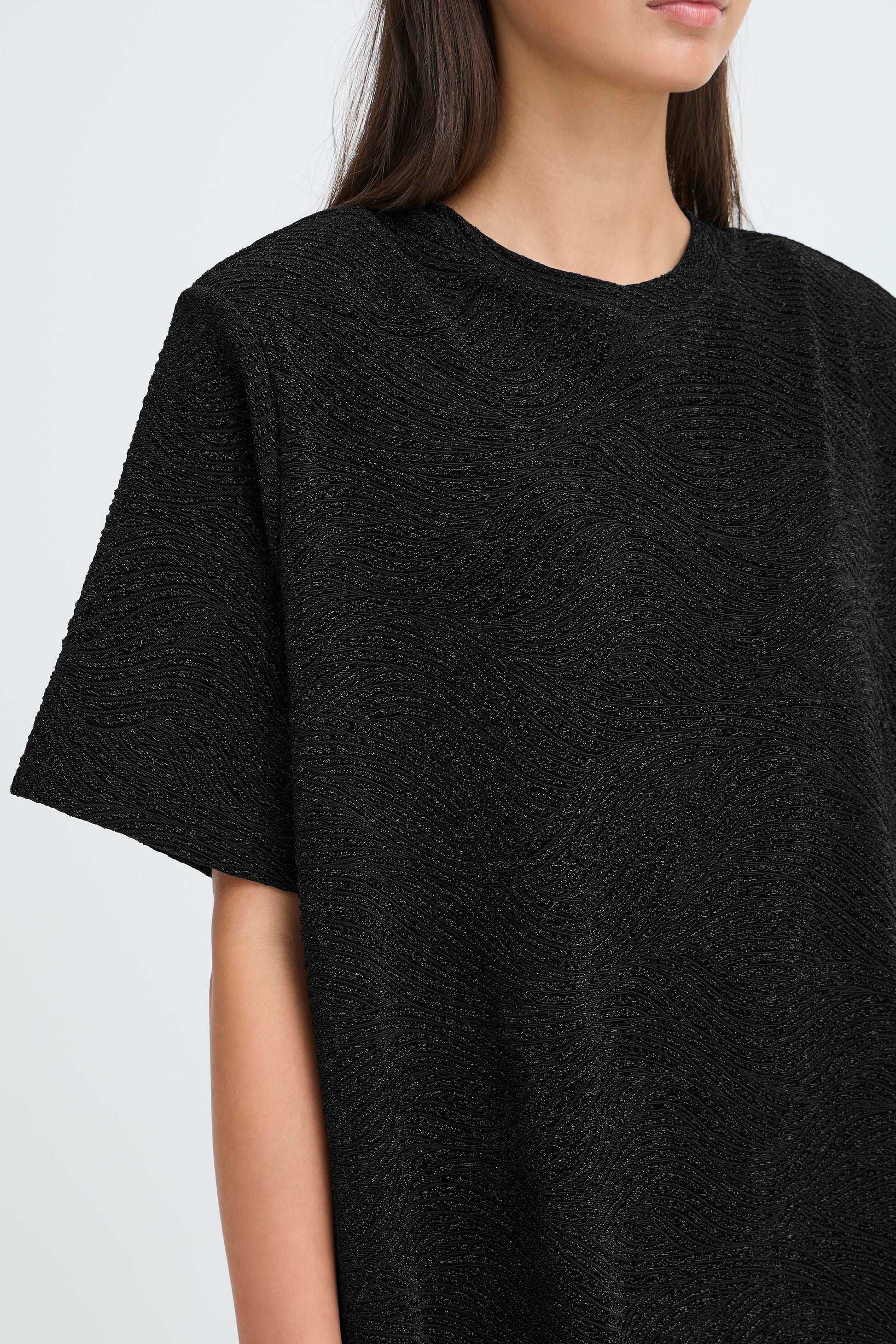 Person wearing a black textured dress against a white background