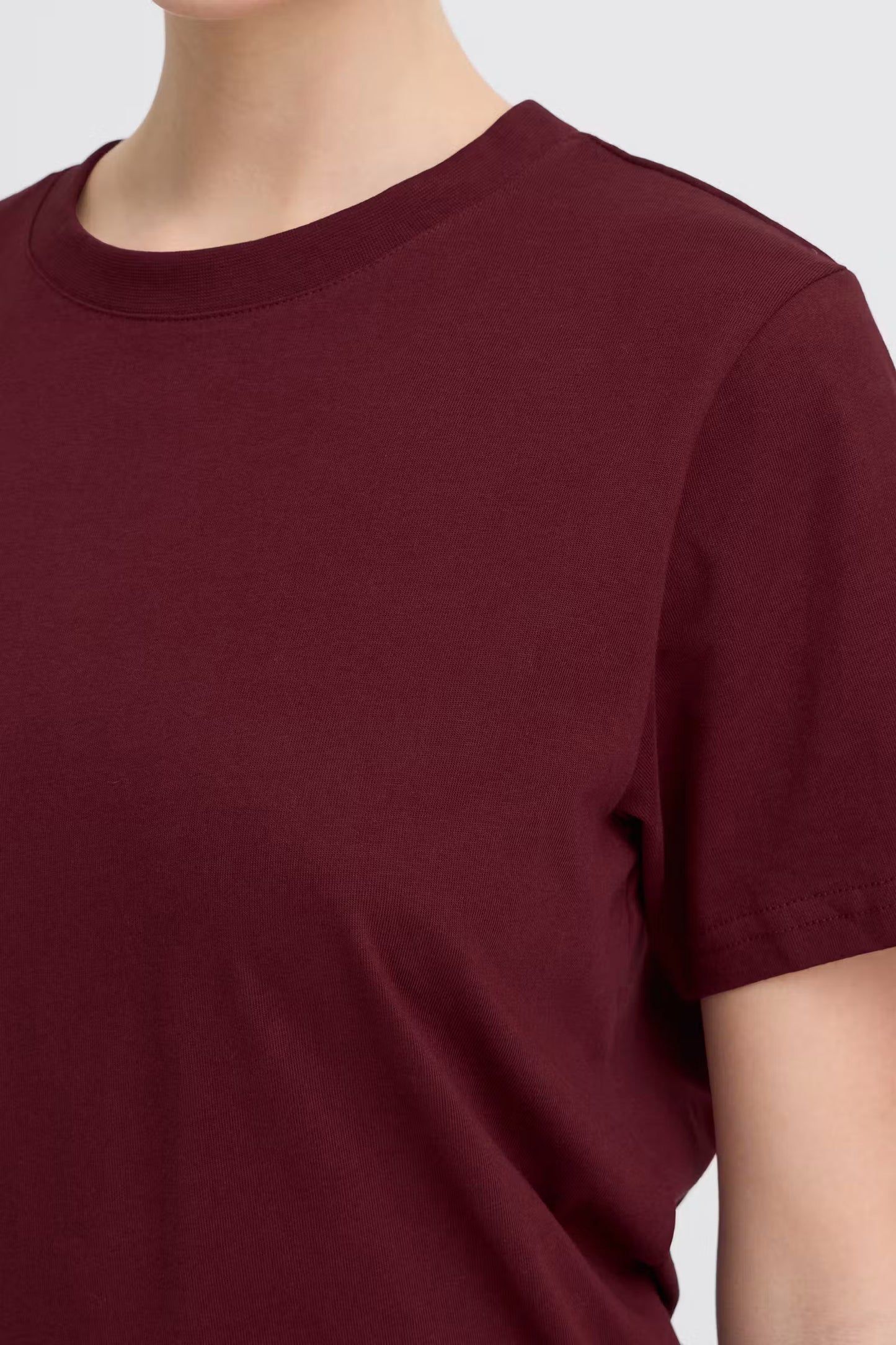 Maroon t-shirt worn by a person on a light gray background