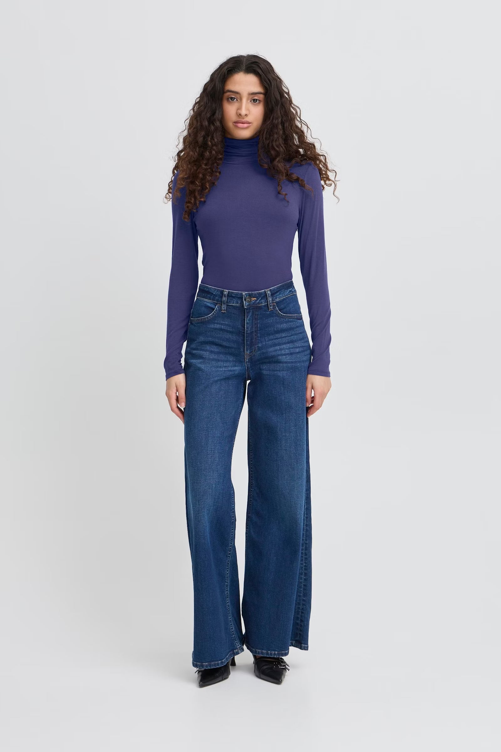 Woman wearing a purple turtleneck and blue jeans on a white background