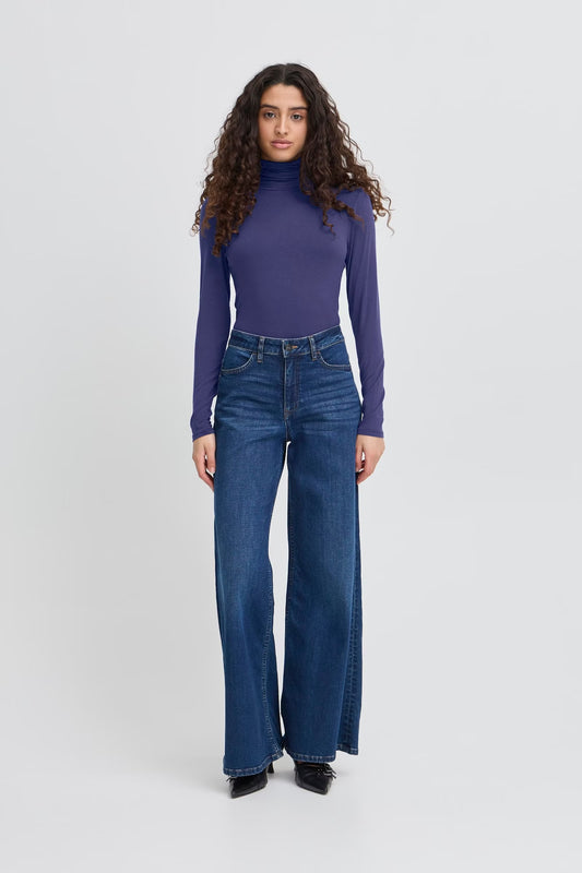 Woman wearing a purple turtleneck and blue jeans on a white background