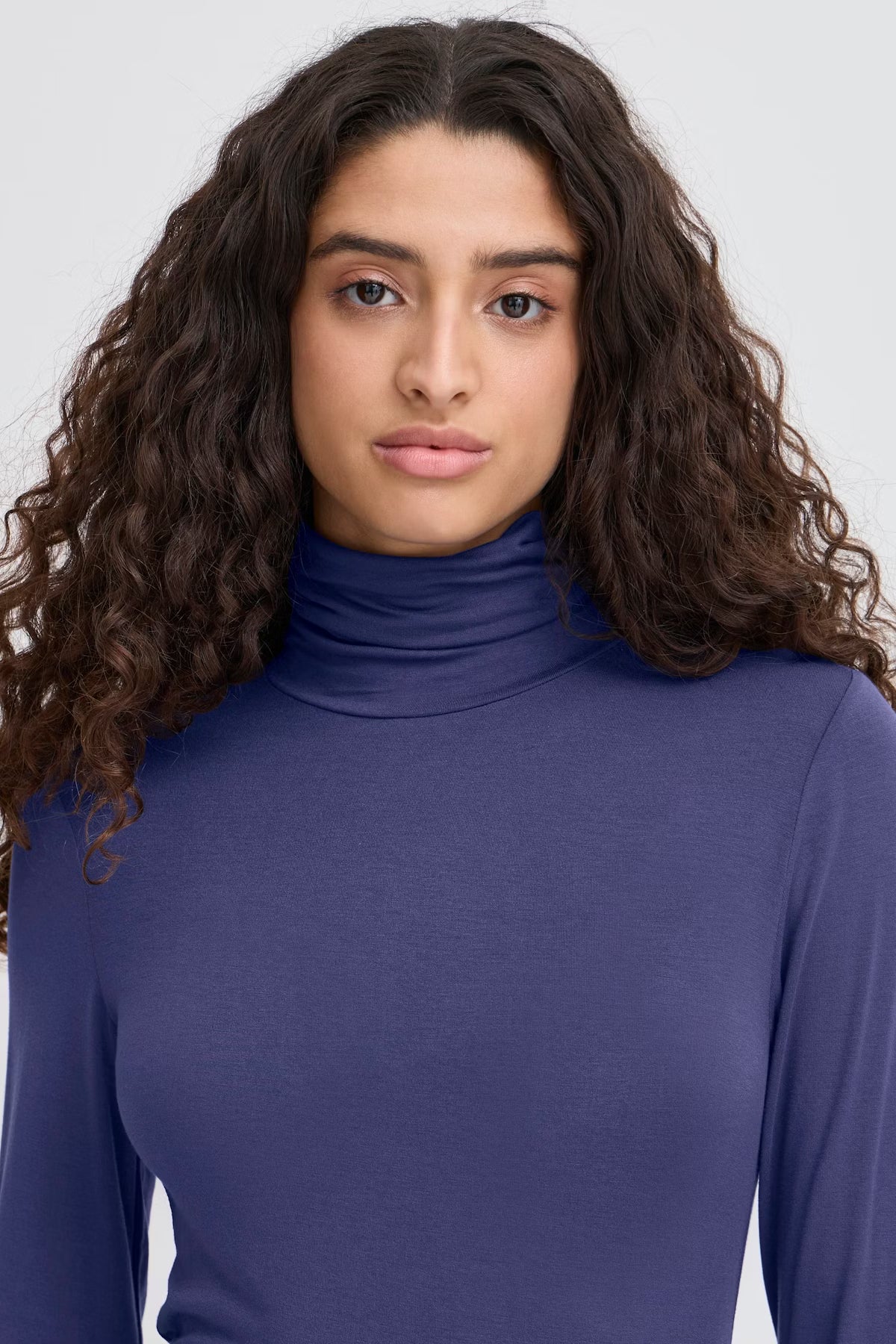 Woman wearing a blue turtleneck against a plain background
