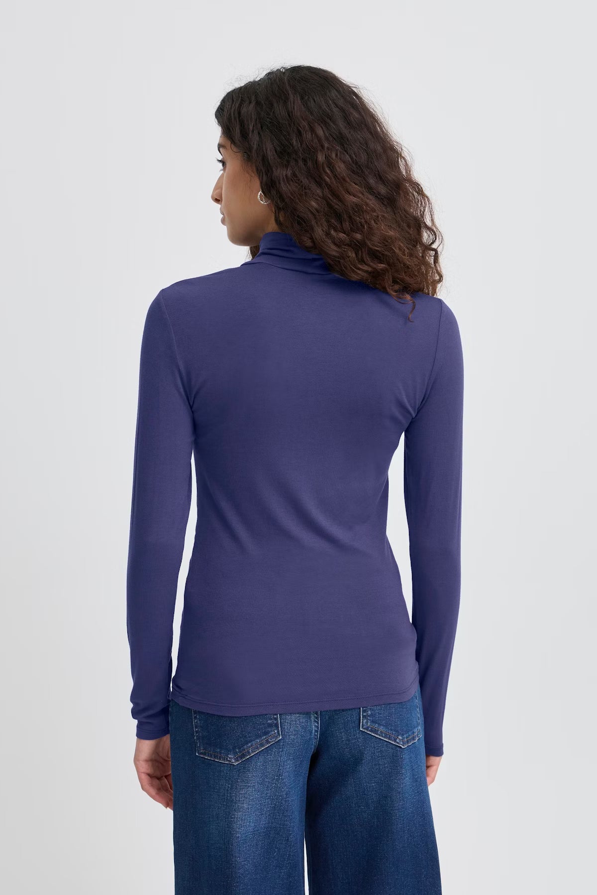 Person wearing a purple long-sleeve top and blue jeans on a white background