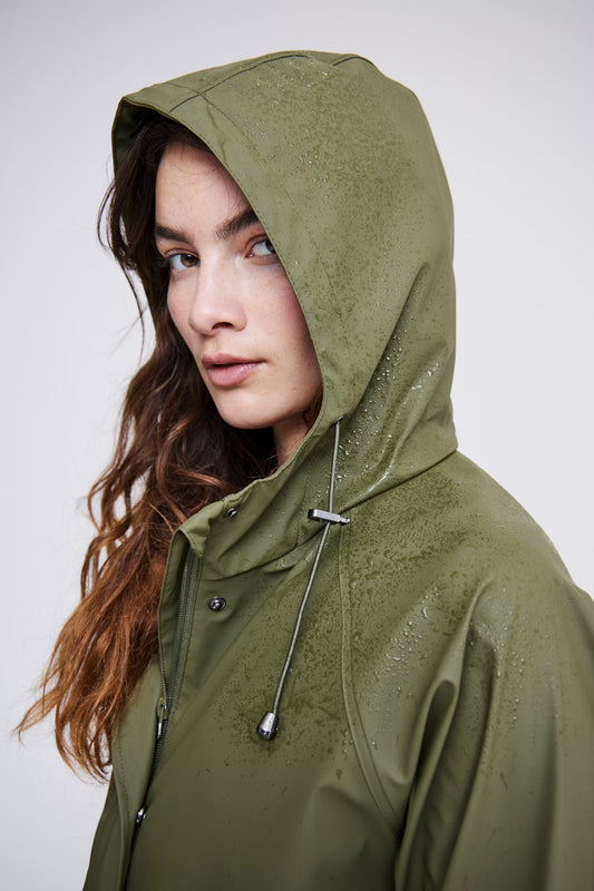 Woman wearing a green raincoat against a plain background