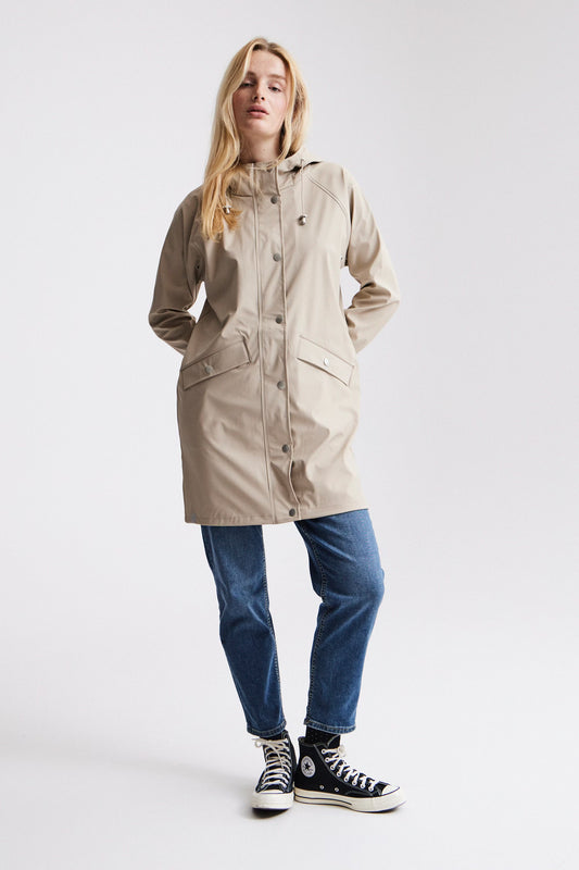 Woman wearing a beige raincoat, blue jeans, and black sneakers on a white background