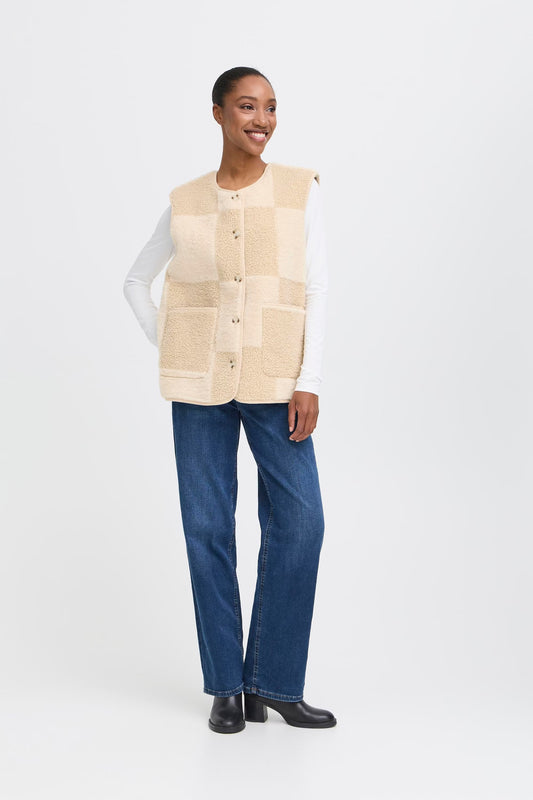 Woman wearing a beige checkered vest over a long-sleeve shirt and blue jeans on a white background