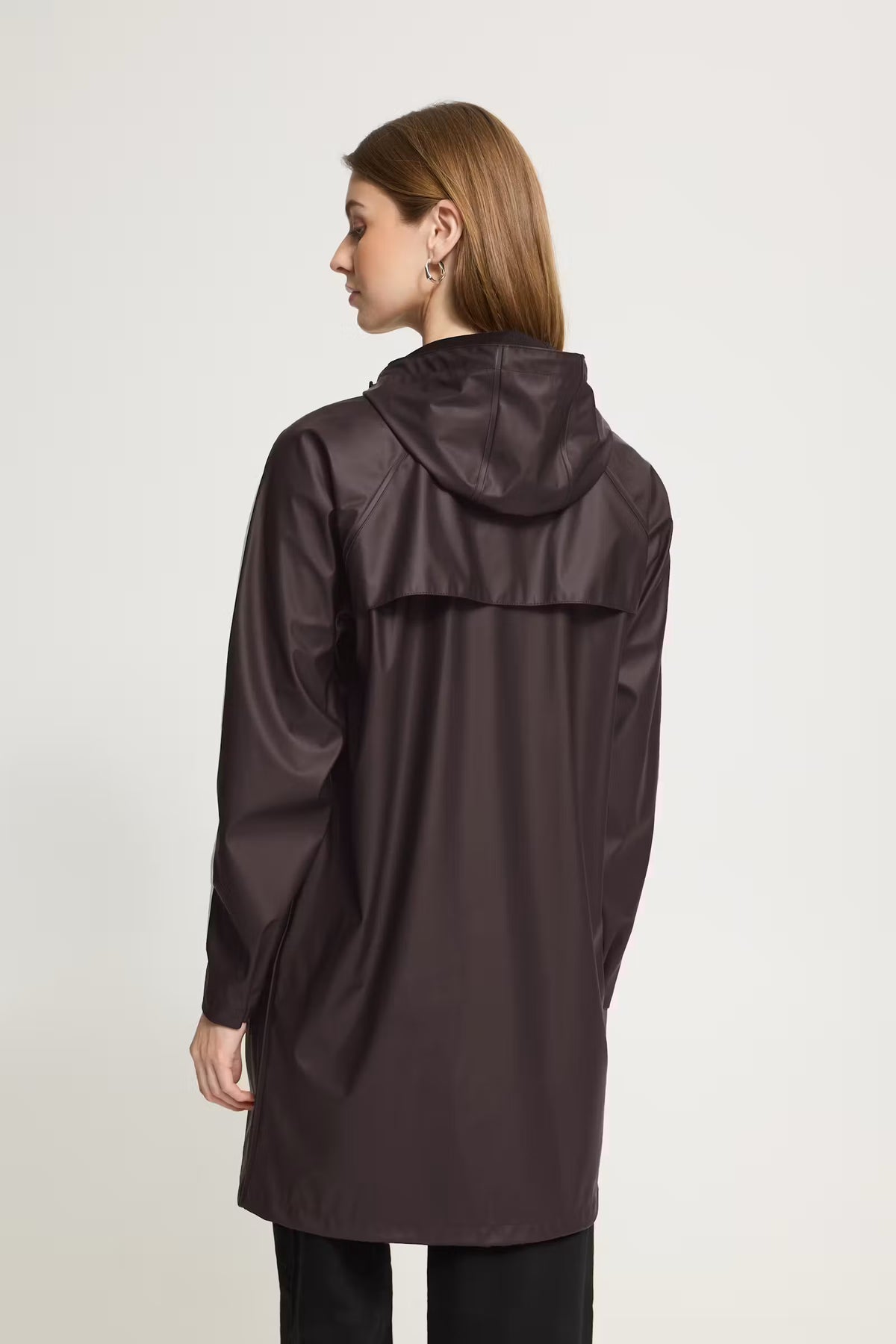 A woman shown from the back wearing a dark brown hooded raincoat against a plain light gray studio background.