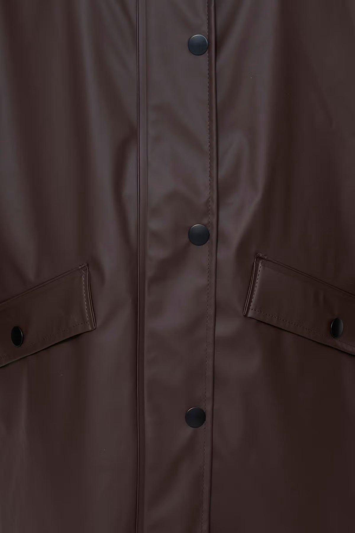 Close-up of a dark brown waterproof jacket featuring a central button closure and two matching flap pockets on the sides.