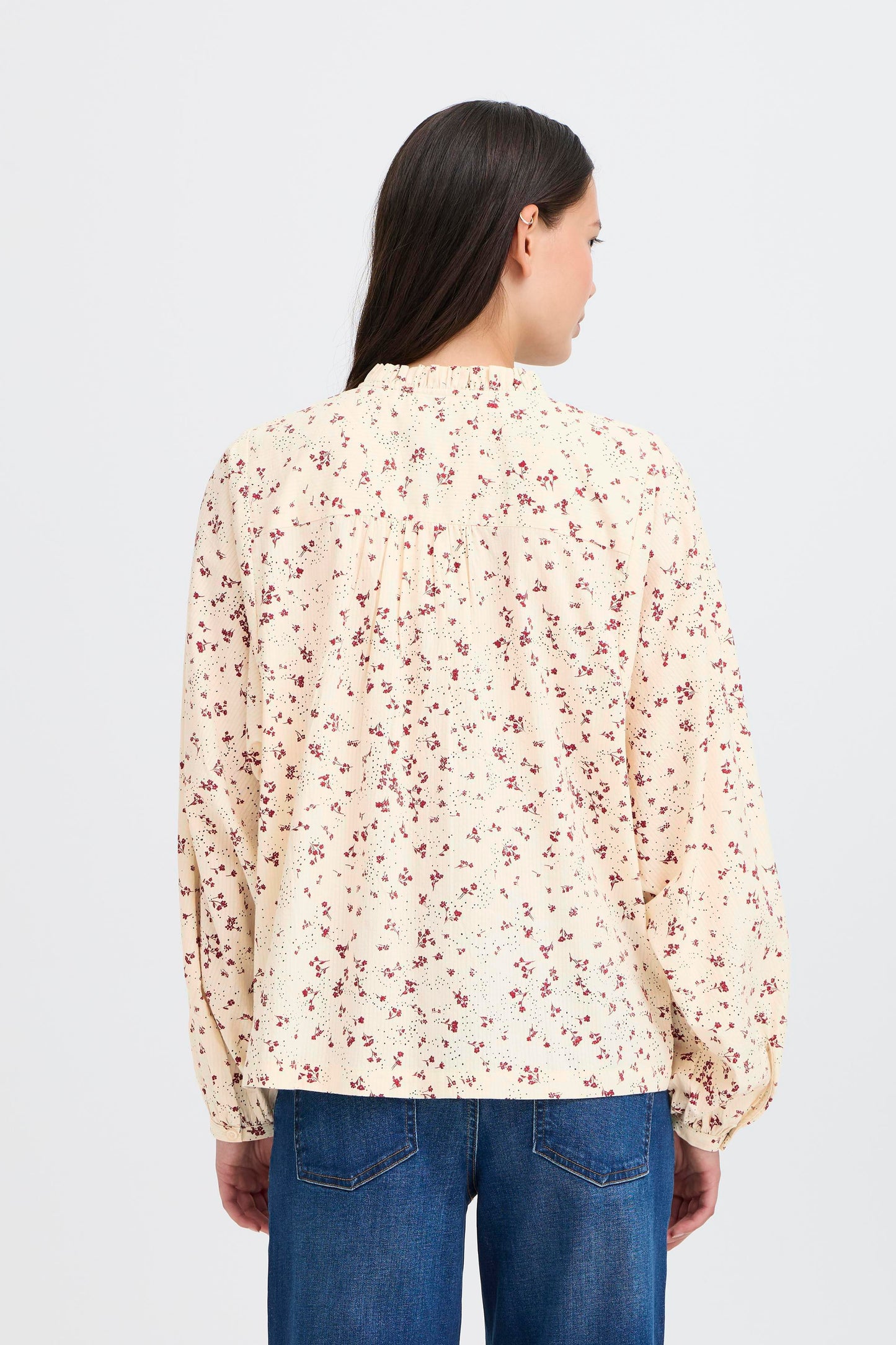 Woman wearing a floral blouse and blue jeans on a light gray background