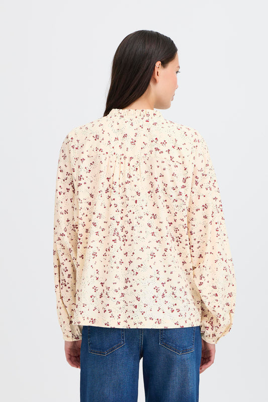 Woman wearing a floral blouse and blue jeans on a light gray background