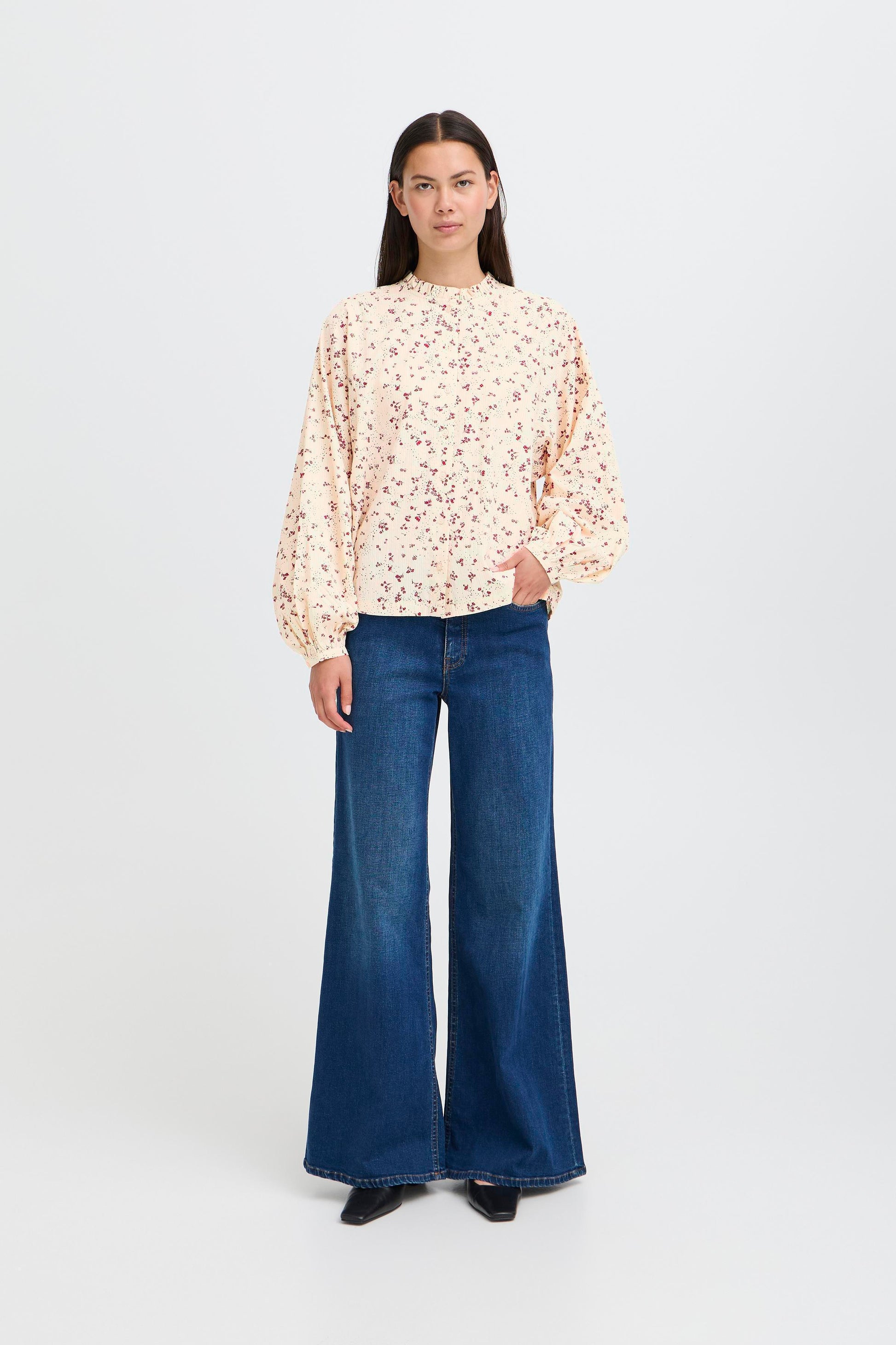 Woman wearing a floral blouse and blue jeans on a white background
