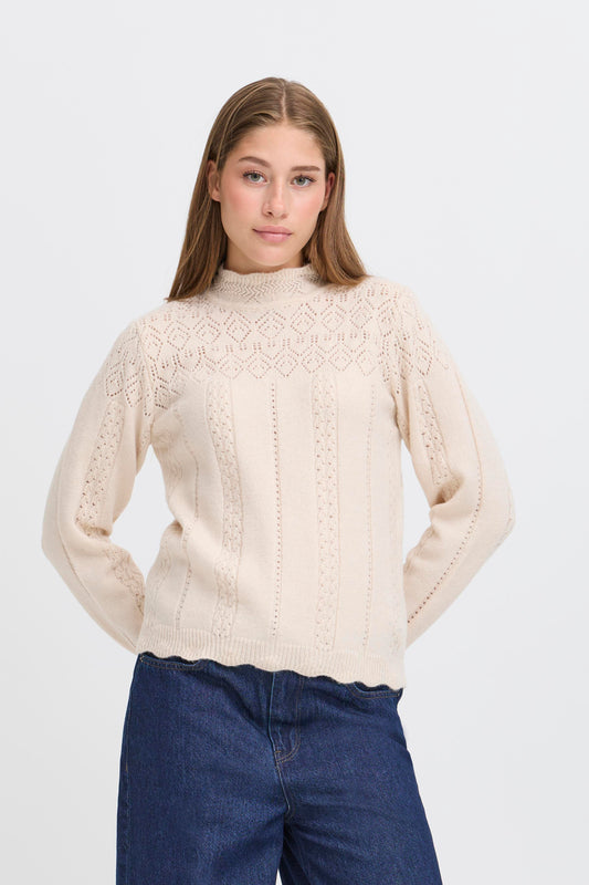 Woman wearing a beige knitted sweater and blue jeans on a white background