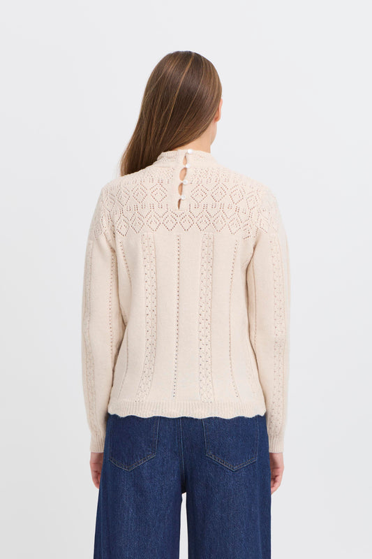Woman wearing a cream knitted sweater and blue jeans on a white background