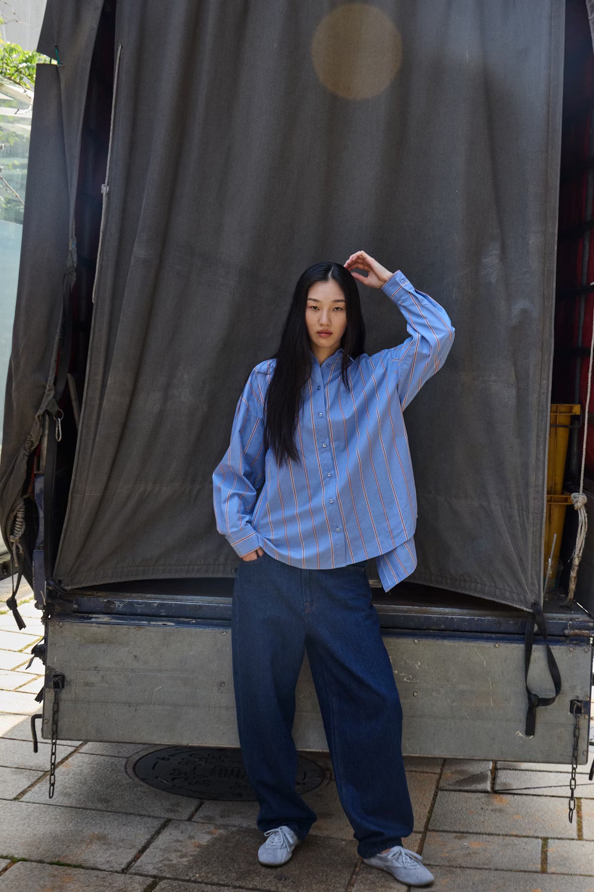 Person wearing a blue striped shirt and jeans standing in front of a large gray curtain.
