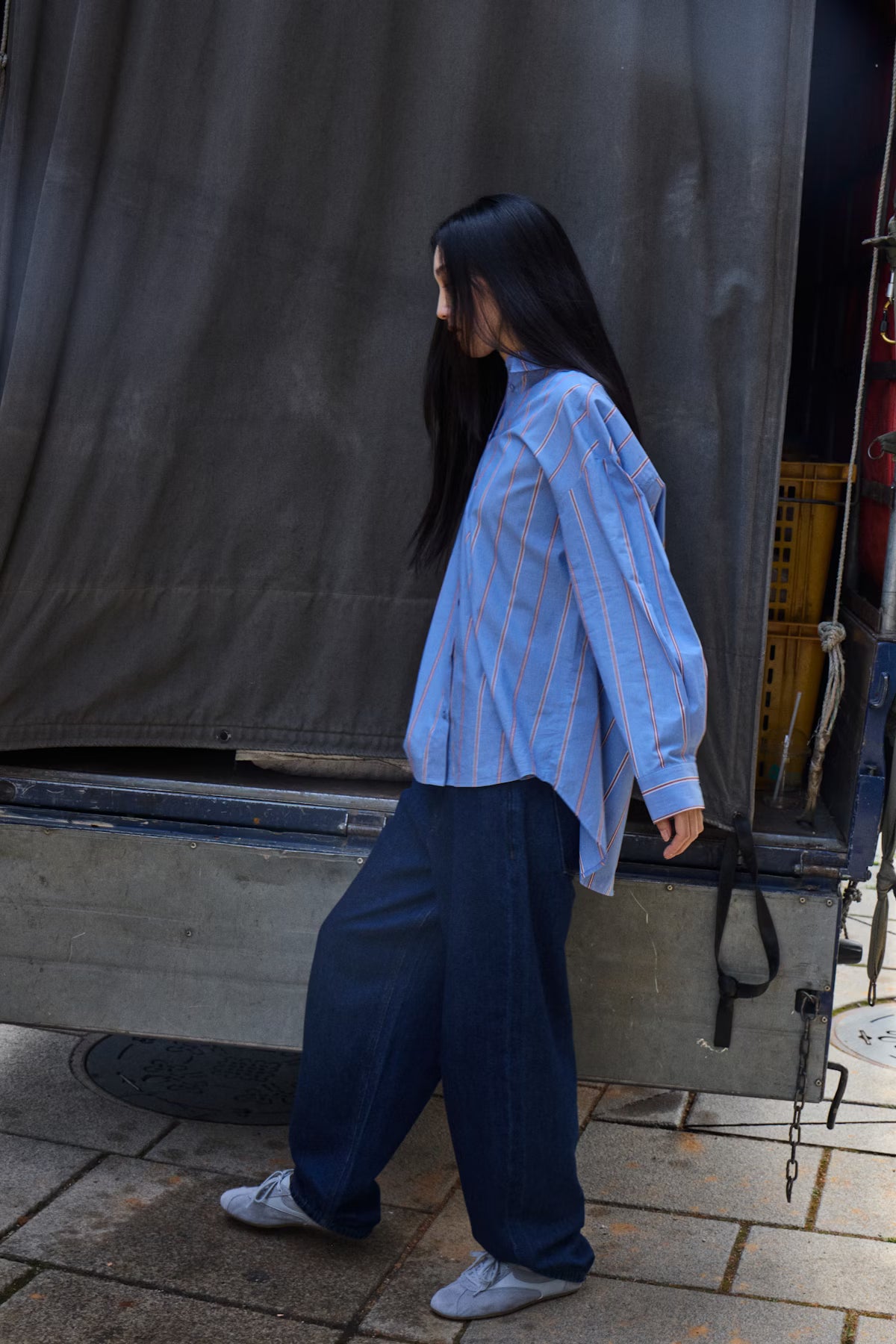 Person wearing a blue striped shirt and dark pants standing next to a vehicle.