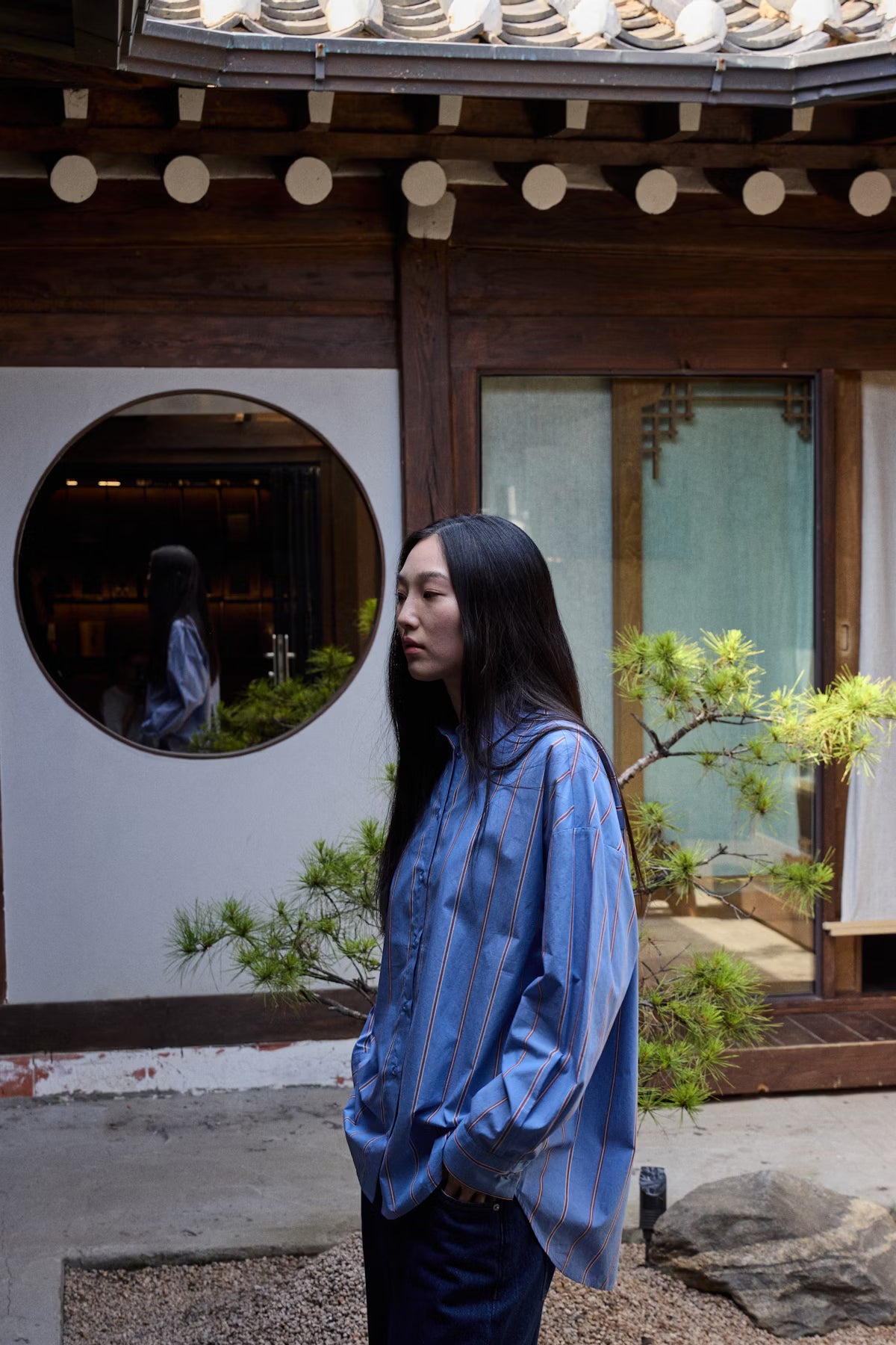Woman in a blue striped shirt standing in a traditional Japanese courtyard.