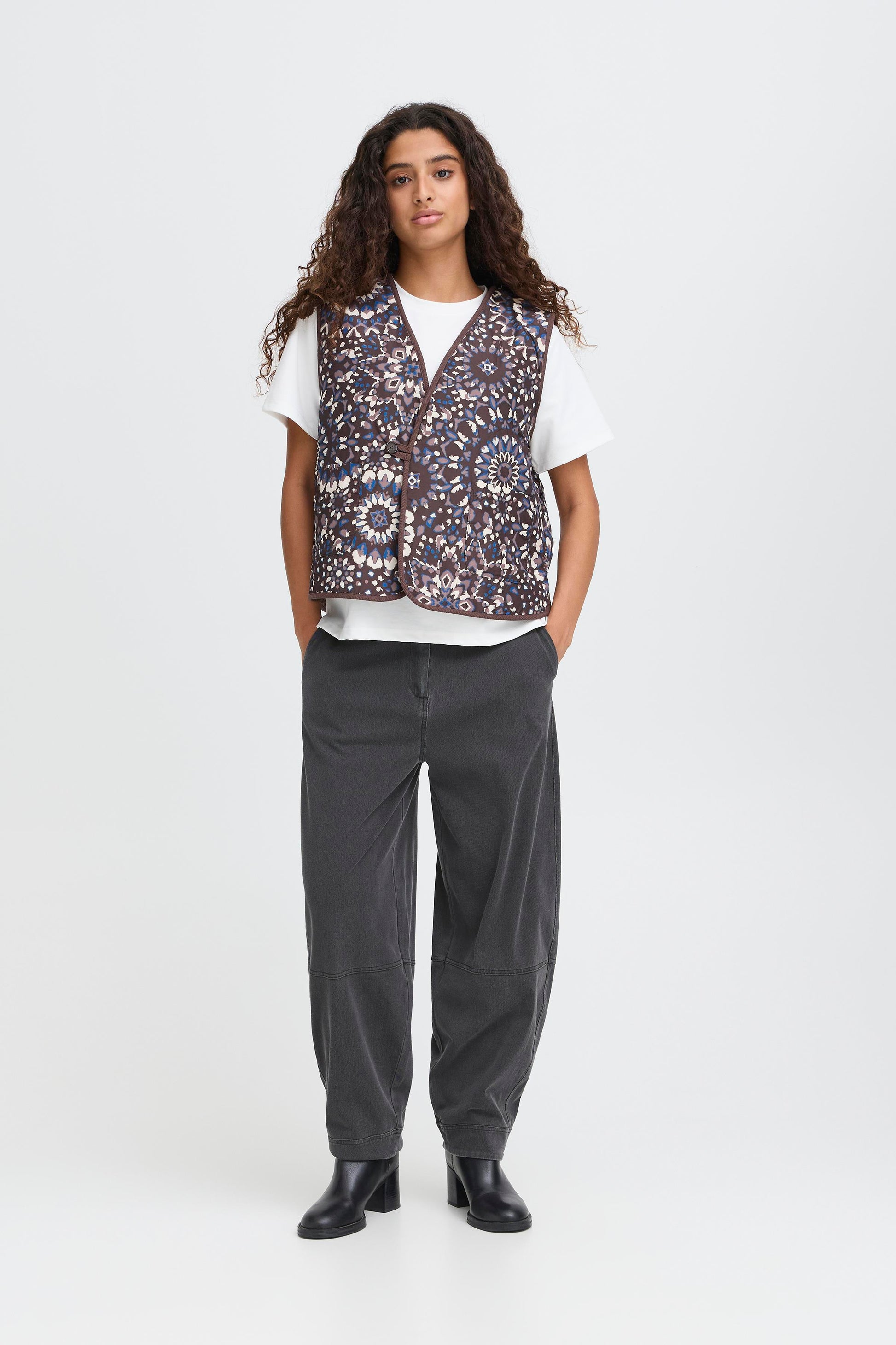 Person wearing a patterned vest over a white shirt with gray pants on a white background