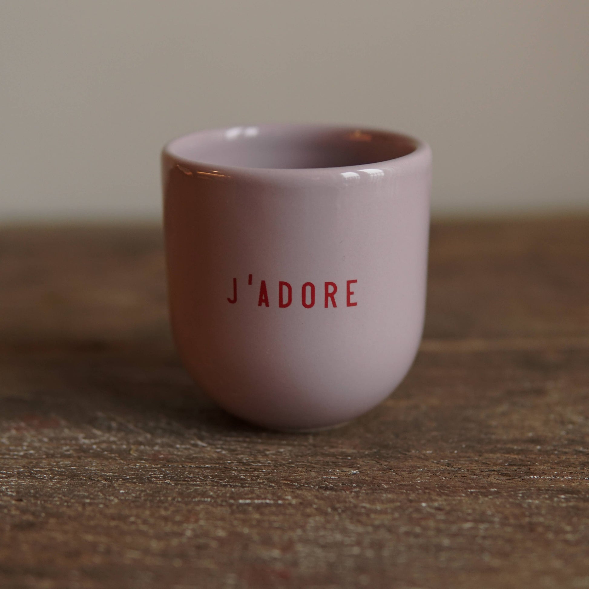 Pink ceramic cup with 'J'ADORE' text on a wooden surface