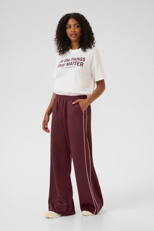 Woman wearing a white t-shirt with text and maroon pants on a white background